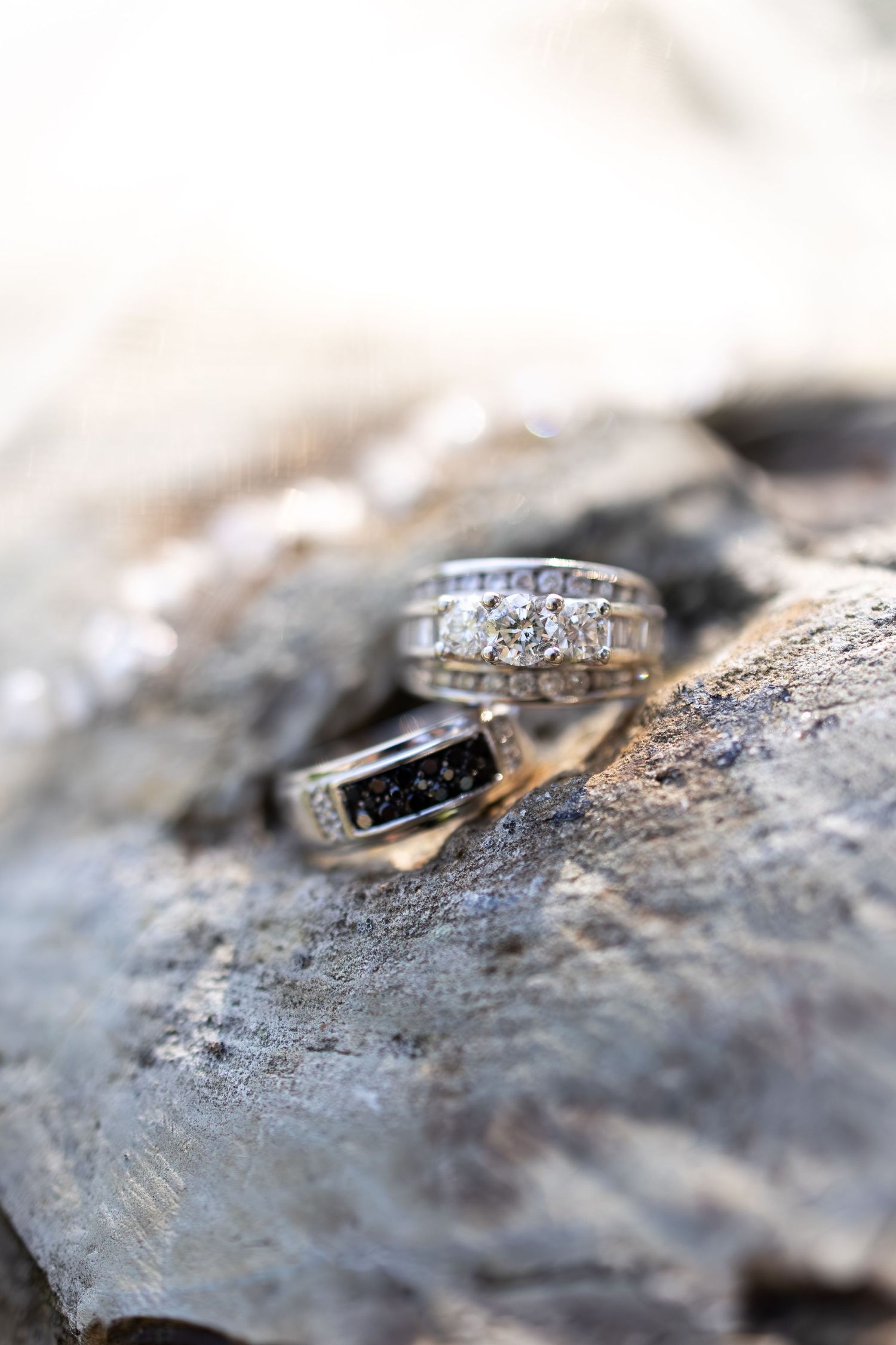 Two diamond wedding rings resting on a rustic rock surface, showcasing intricate silver band designs.