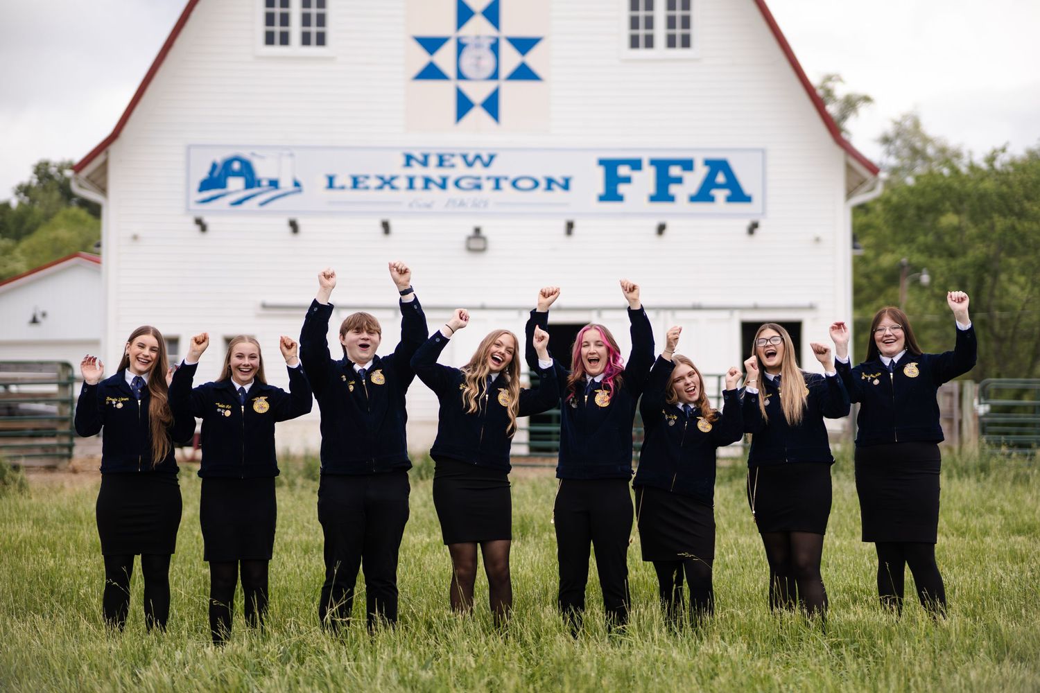 New Lexington FFA students celebrating with raised arms in front of their chapter barn.