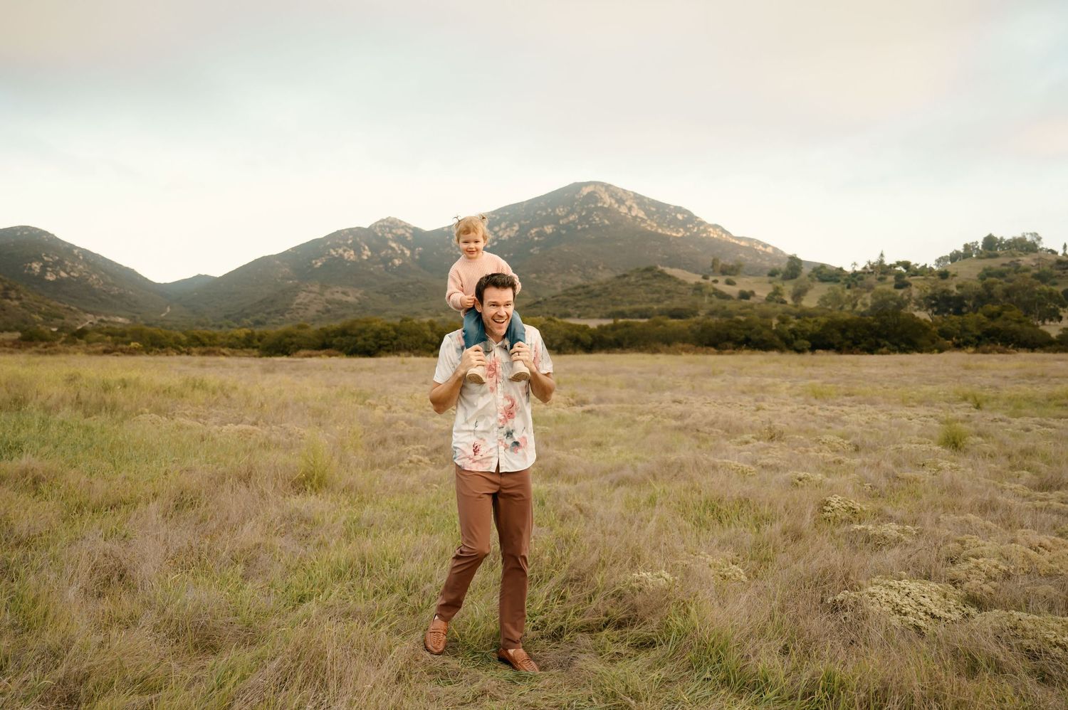 family photoshoot of dad with baby girl on shoulders in grassy field by Ventura county photographer