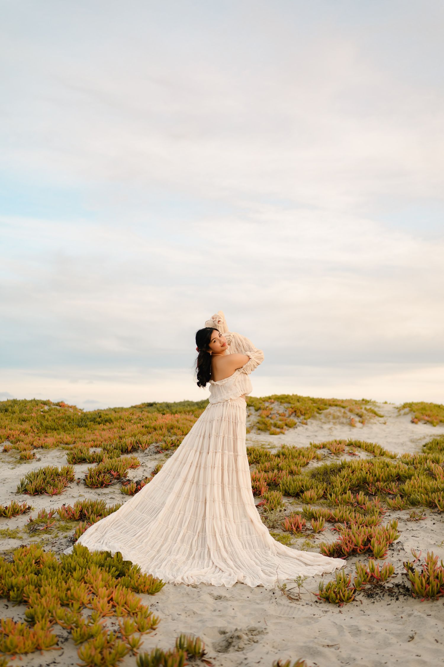 high school senior girl in beautiful dress standing on succulent covered sand dunes during her senior portraits by Ventu
