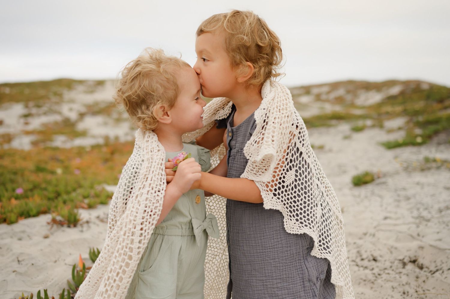 young sisters embracing and giving each other a kiss during their beach family photoshoot by Ventura County photographer