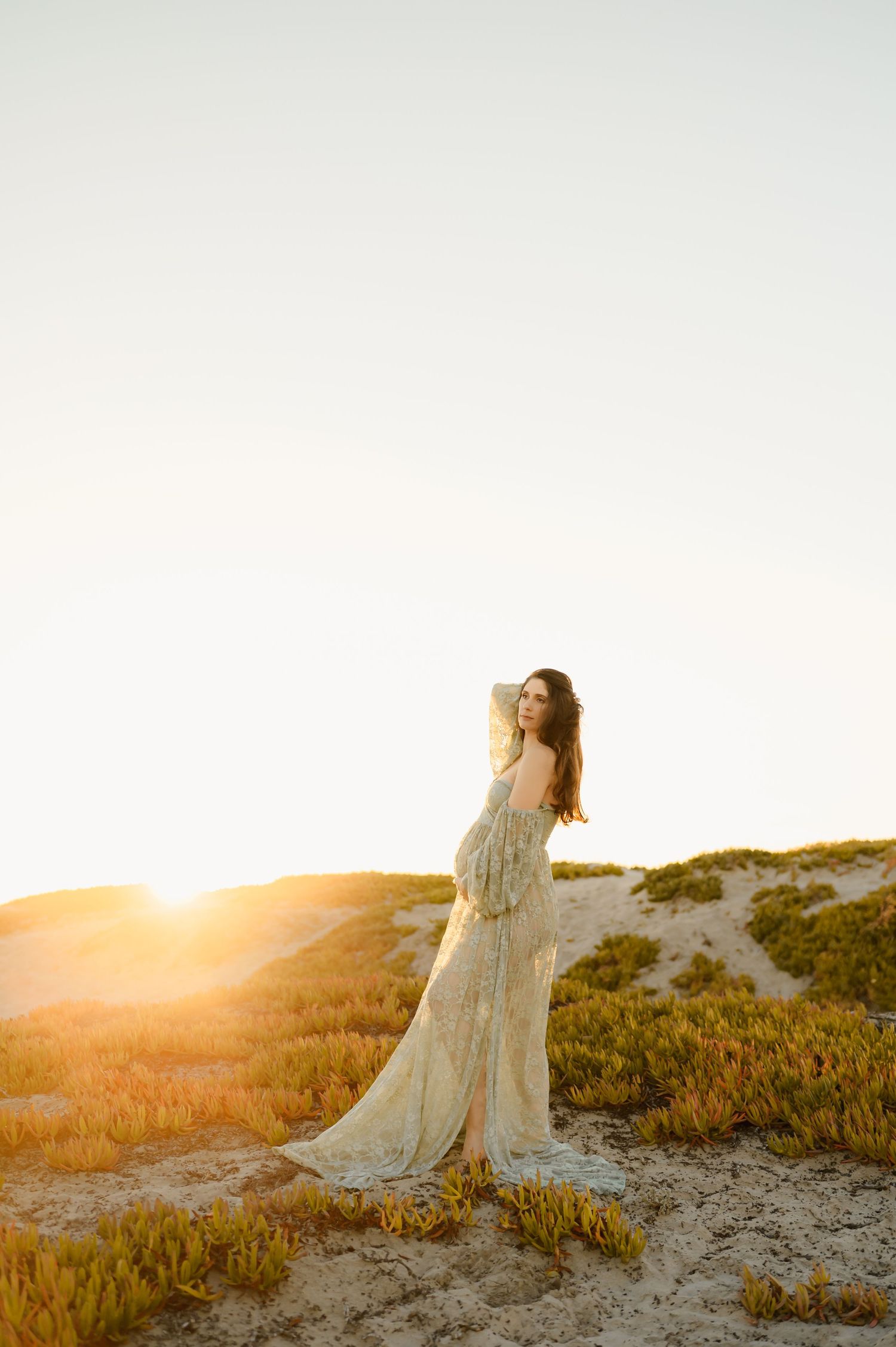 Woman in a flowing dress standing on Oxnard sand dunes at sunset by Ventura maternity photographer