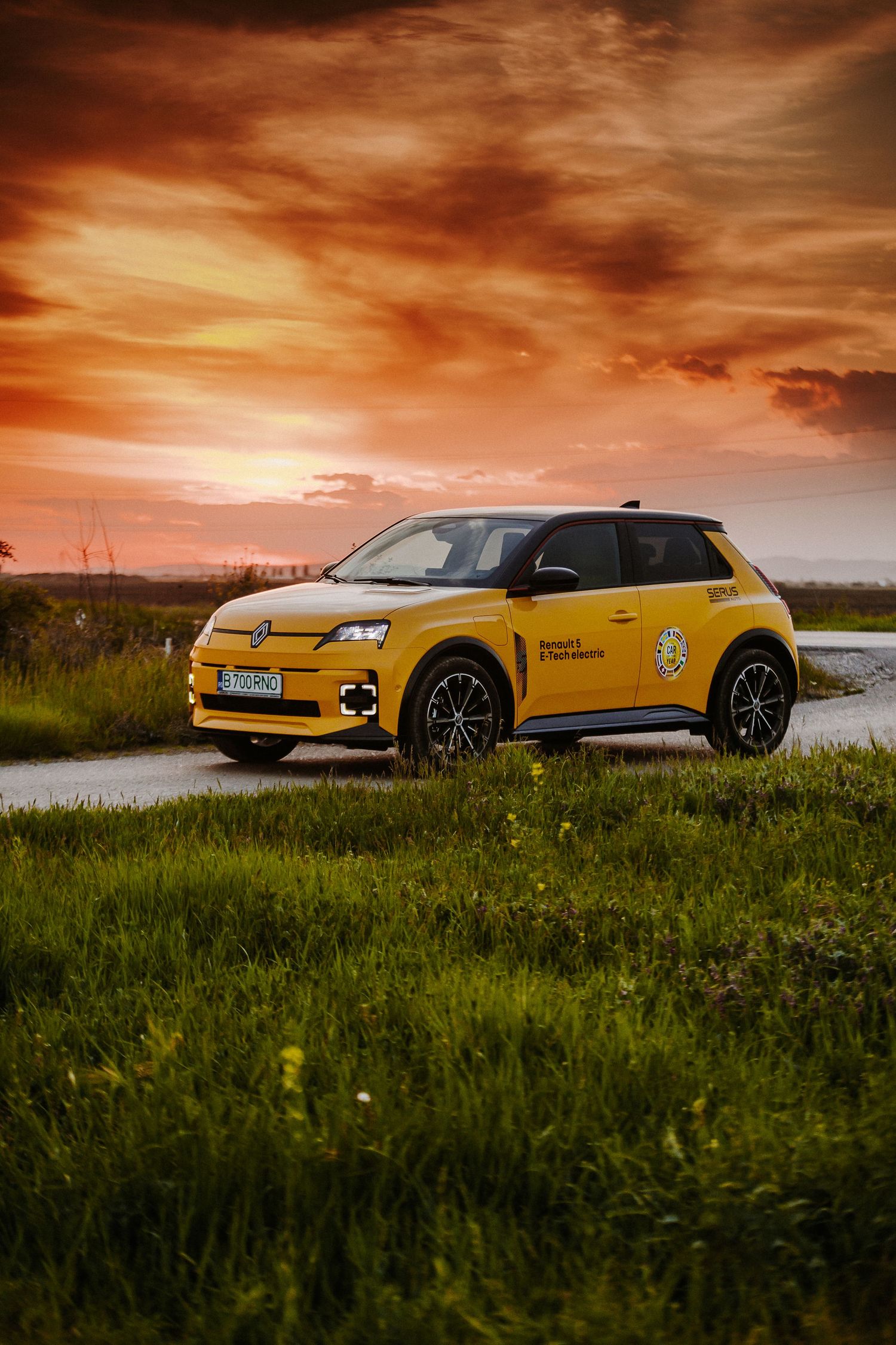 Yellow Renault 5 electric car parked on a rural road at sunset with dramatic orange cloudy sky.