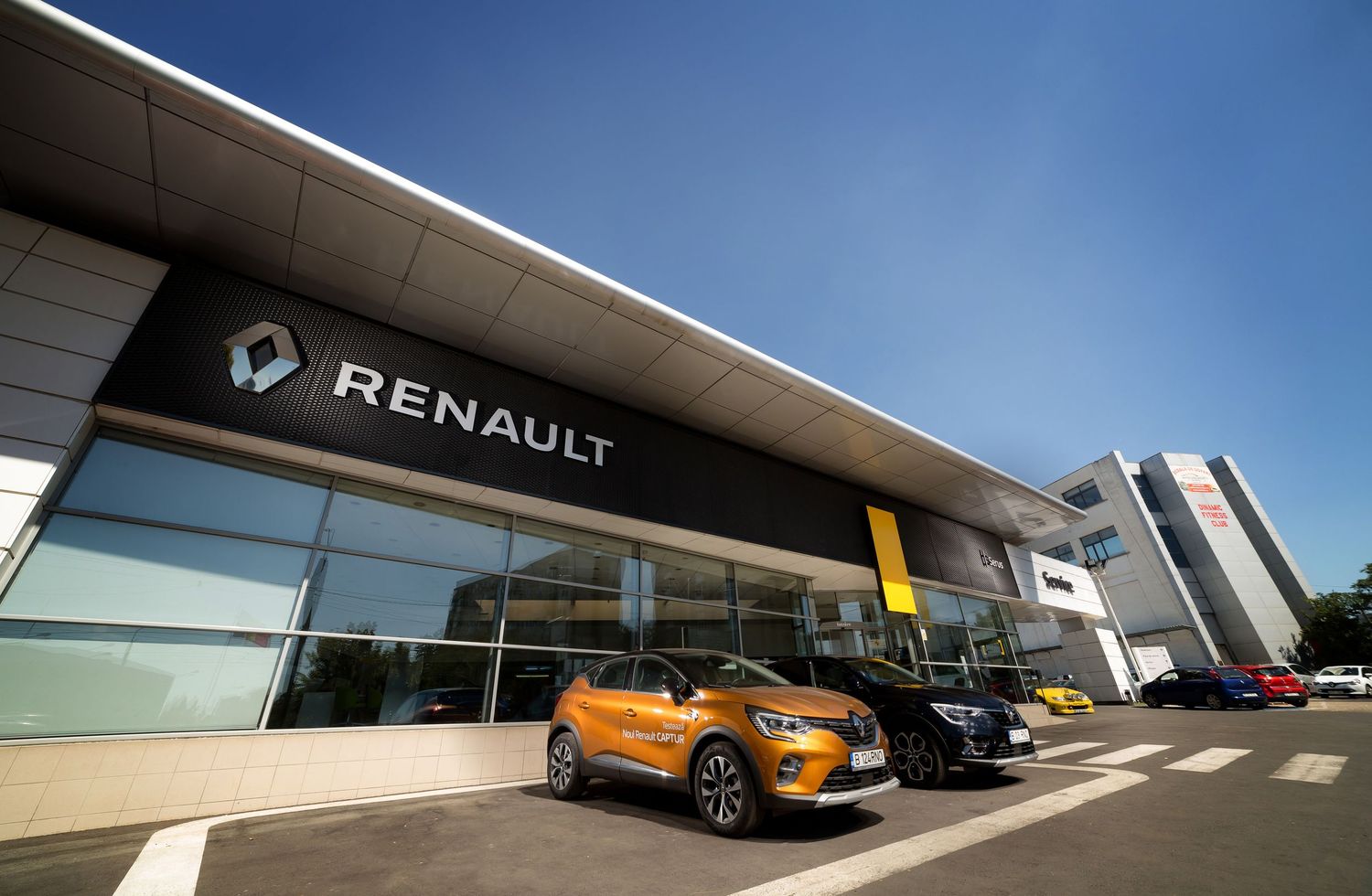 Modern Renault car dealership exterior with orange SUV displayed under bright blue sky.