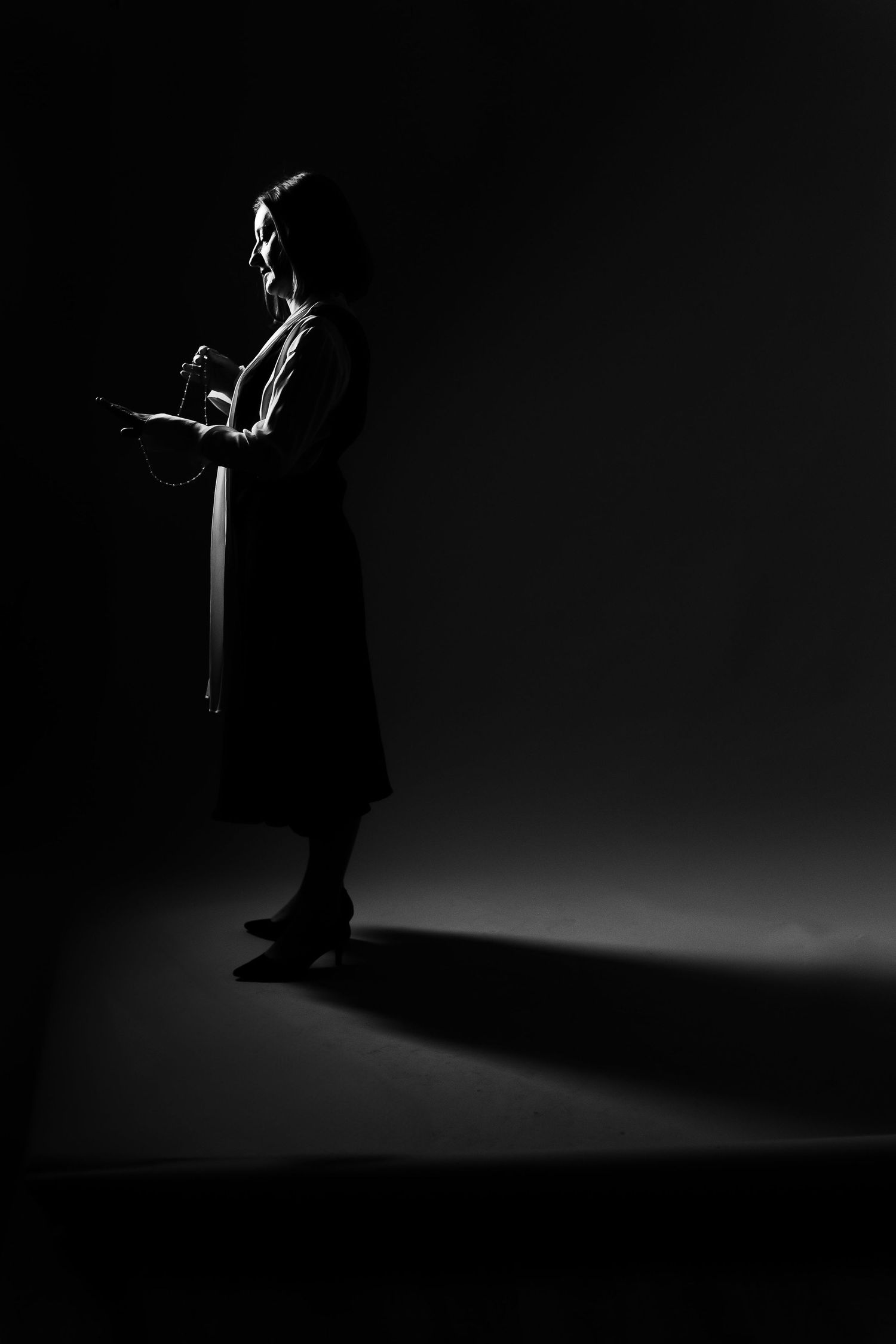 Dramatic black and white silhouette of a woman holding a bag, casting a long shadow on a dark studio background.