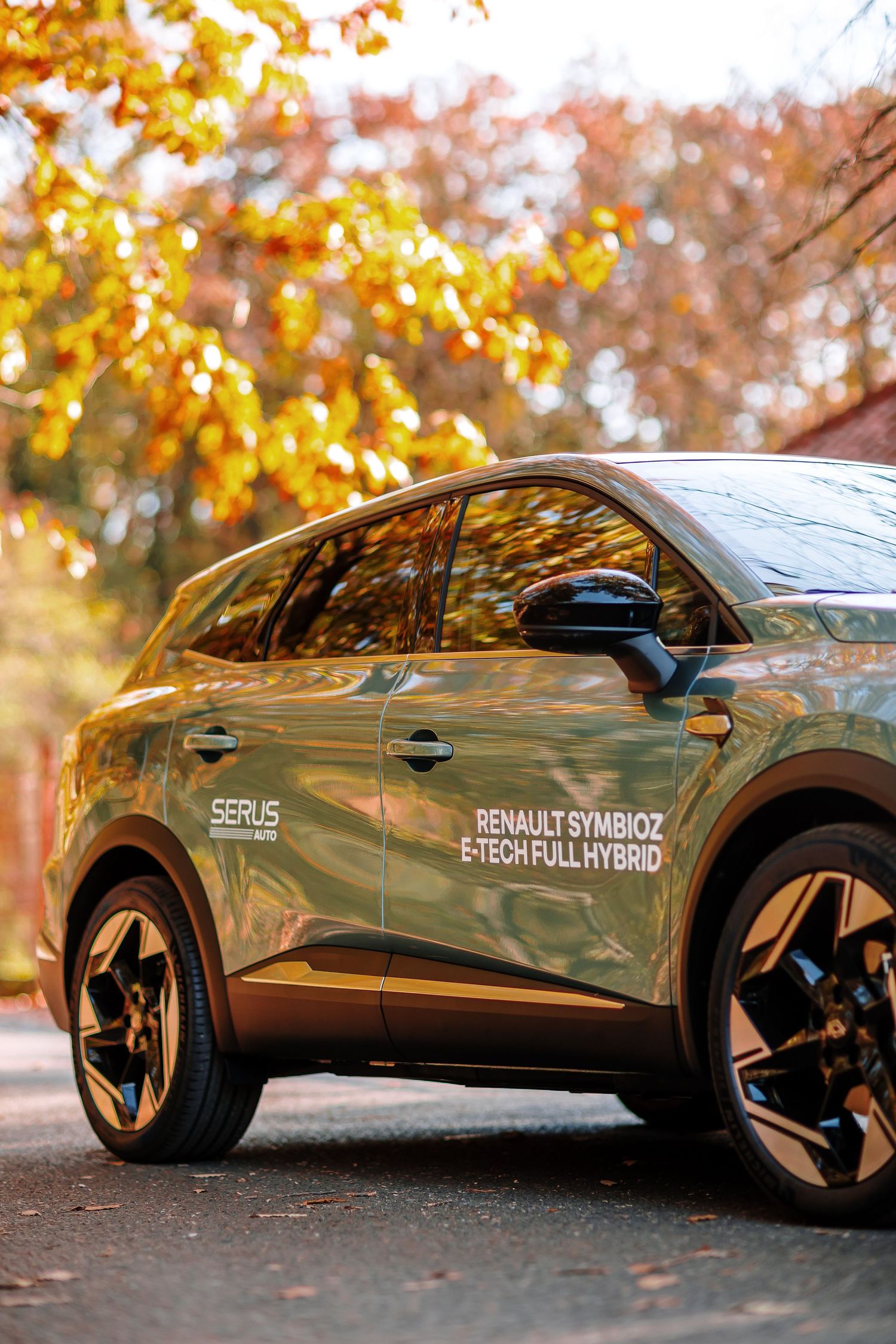 Renault Symbioz E-Tech Full Hybrid SUV in olive green, parked outdoors with autumn foliage in the background.