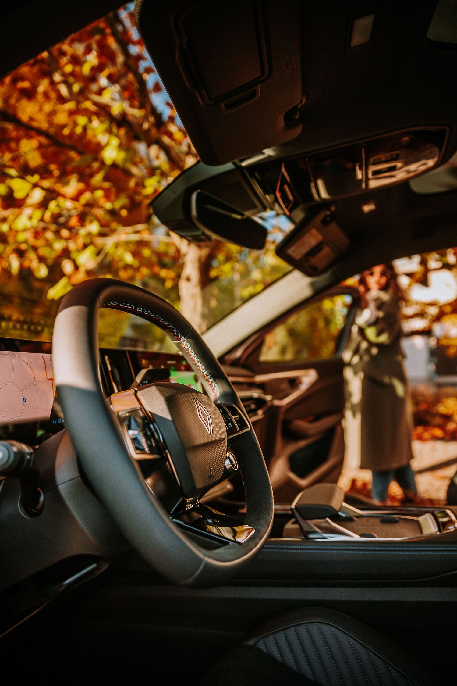Luxury Lincoln car interior with leather steering wheel, viewed from inside with autumn foliage visible through windshield.