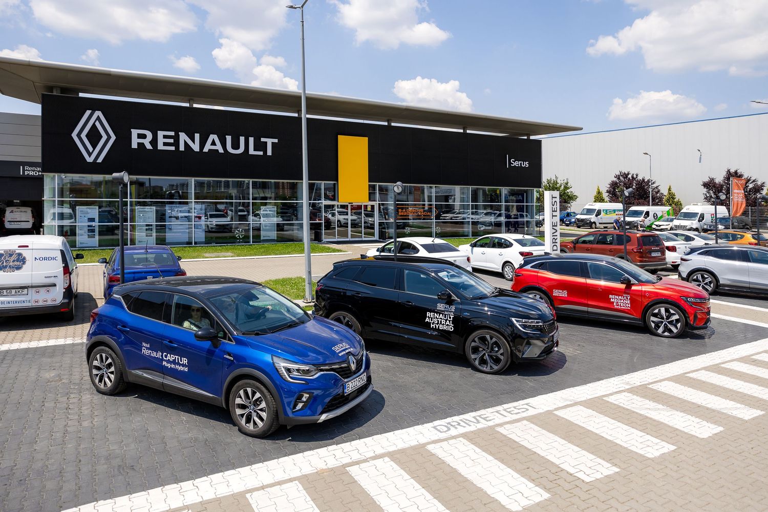 Multiple Renault cars displayed outside a Renault dealership on a sunny day, featuring blue, black, and red models.