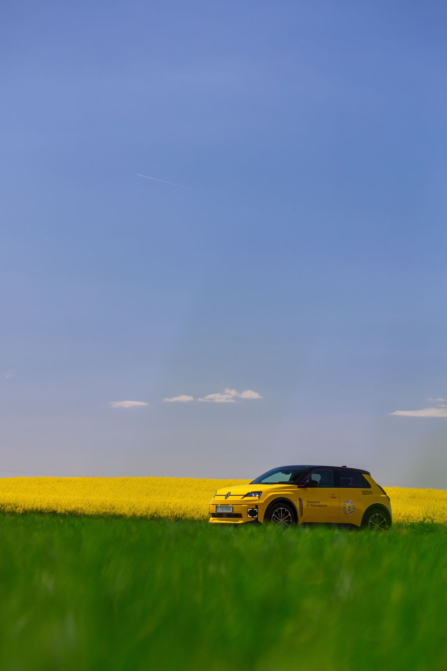 Yellow Renault 5 electric car parked in a vibrant rapeseed field under a clear blue sky.