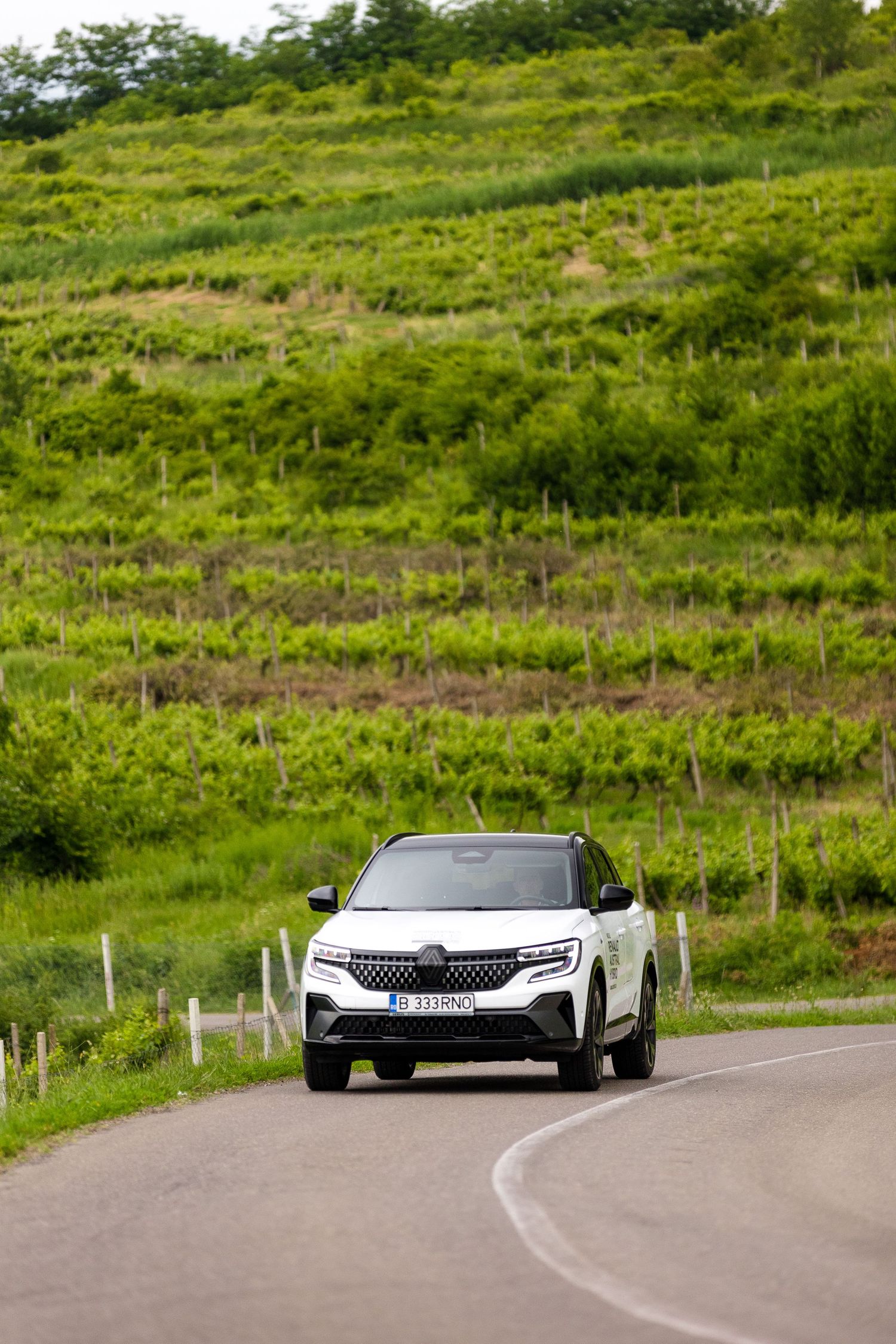 White Renault SUV driving on a winding road surrounded by lush green vineyard hills.