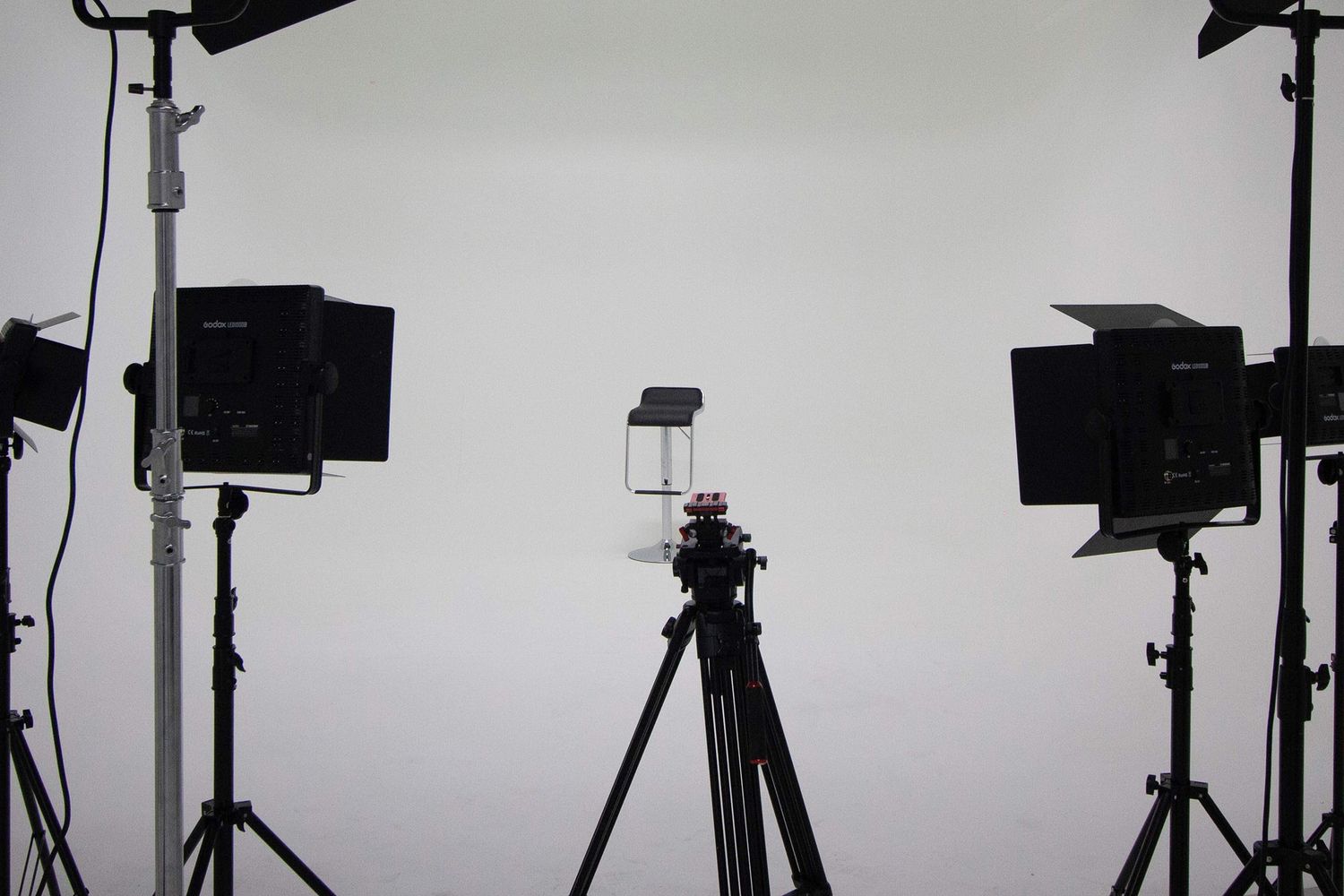 Professional photography studio setup with three light stands and a camera on a tripod against white backdrop.