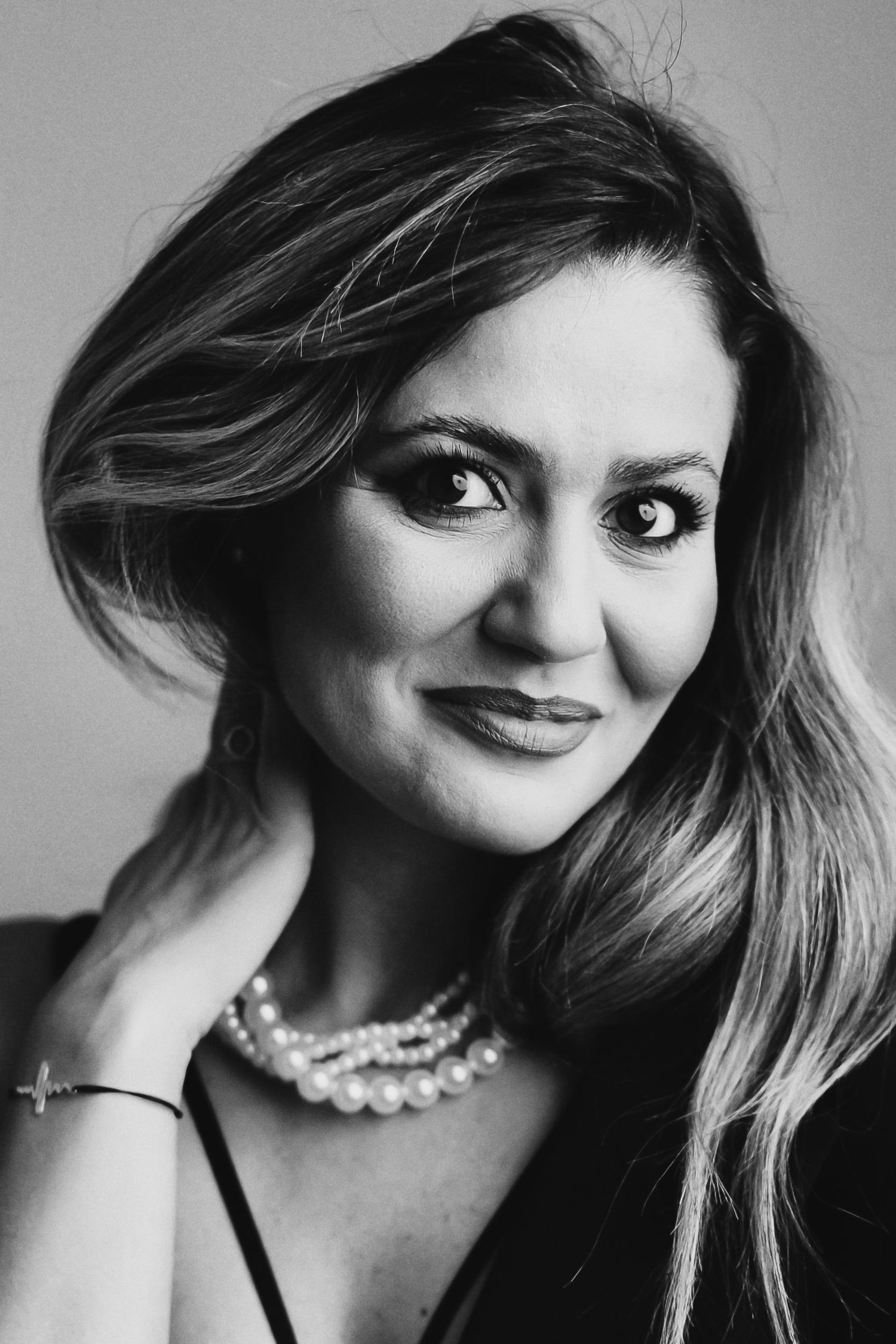 Black and white portrait of a smiling woman wearing a pearl necklace and bracelet with elegant makeup.