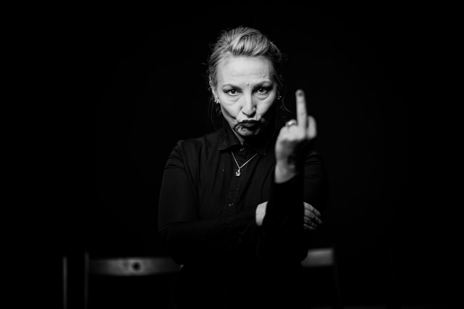 Black and white portrait of a blonde woman in black clothing giving the middle finger gesture.