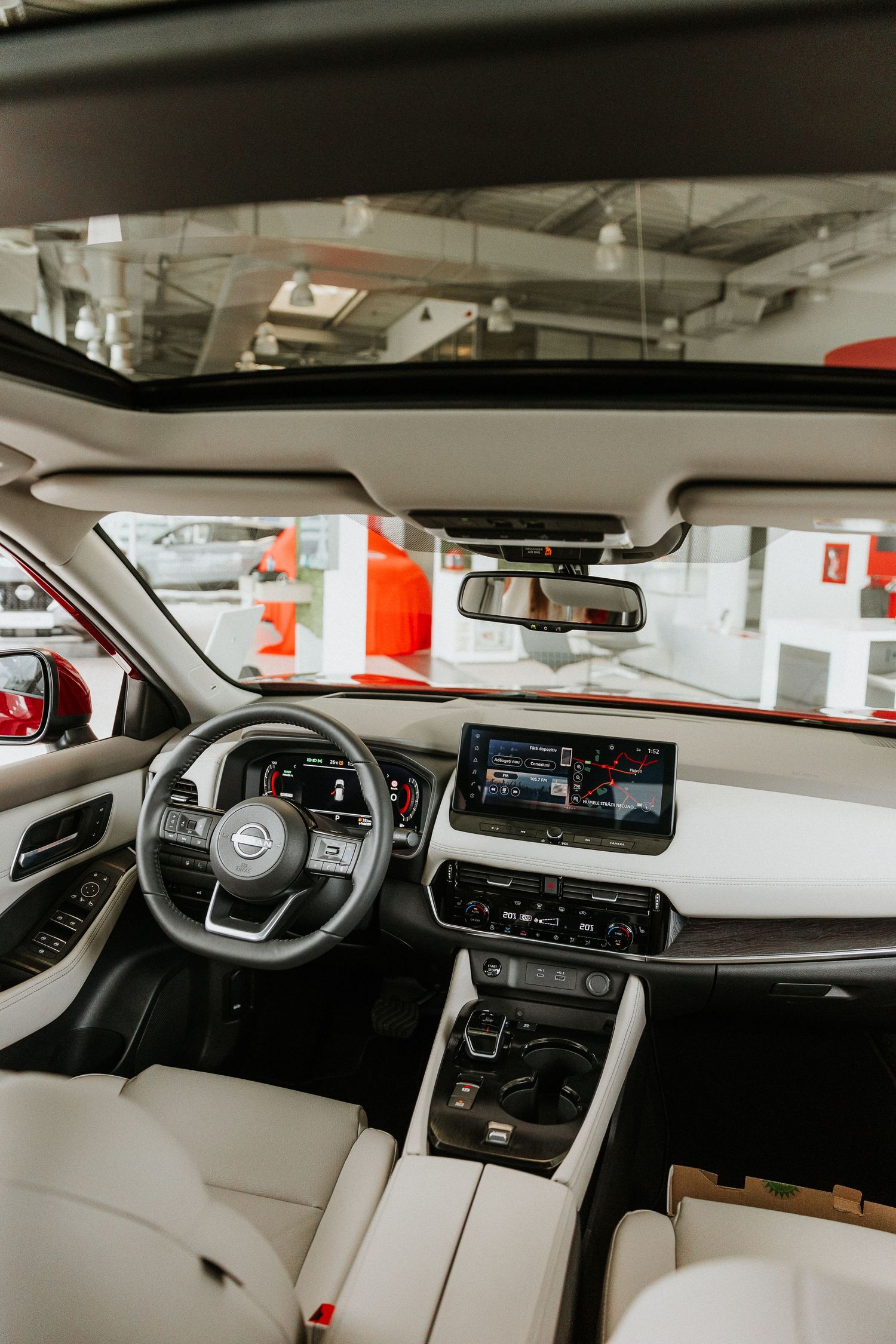 Modern Nissan SUV interior with white leather seats, touchscreen infotainment, sunroof, and steering wheel in a showroom.