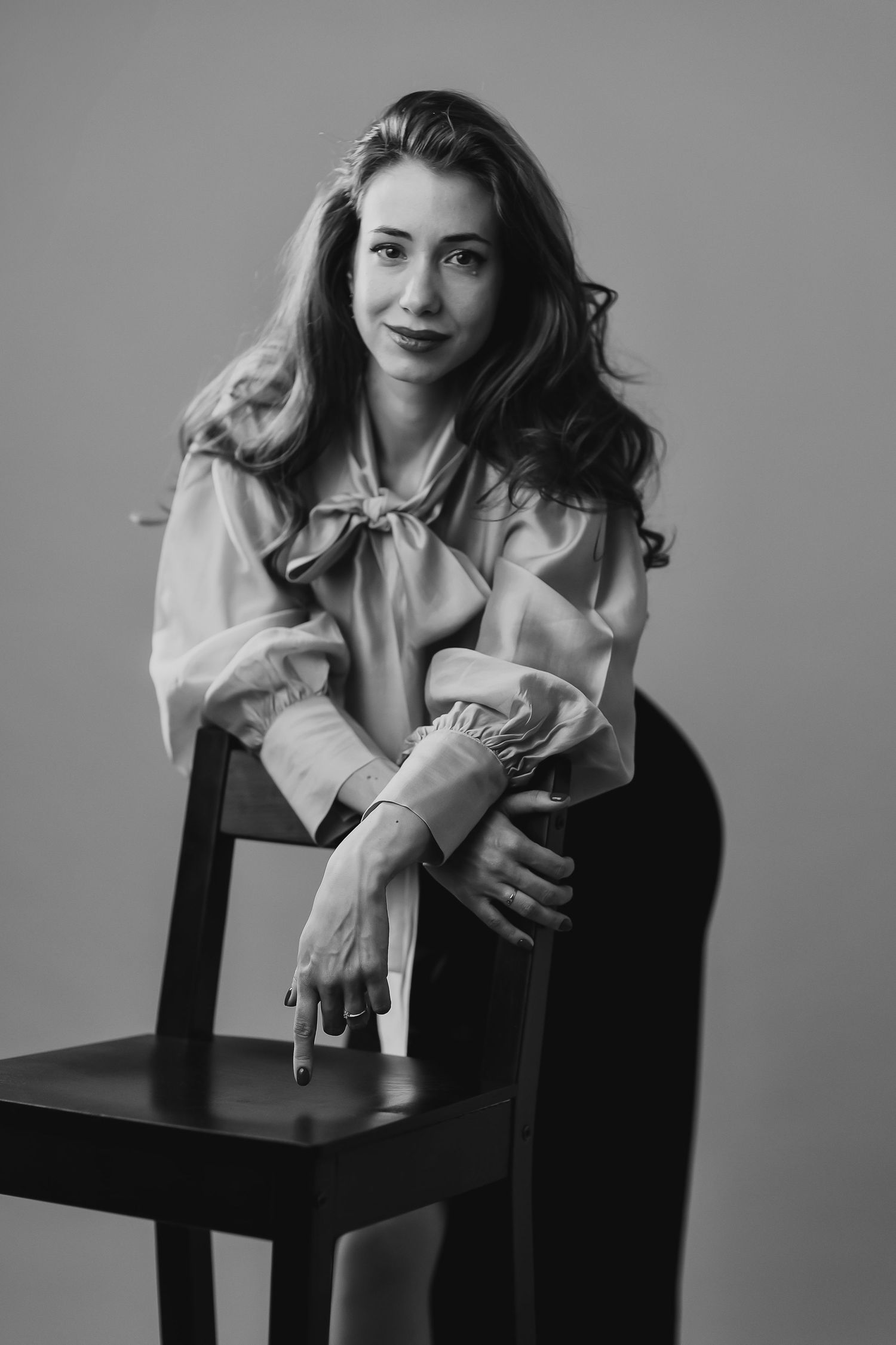 Black and white portrait of a young woman in a ruffled blouse, seated on a chair, smiling softly at the camera.