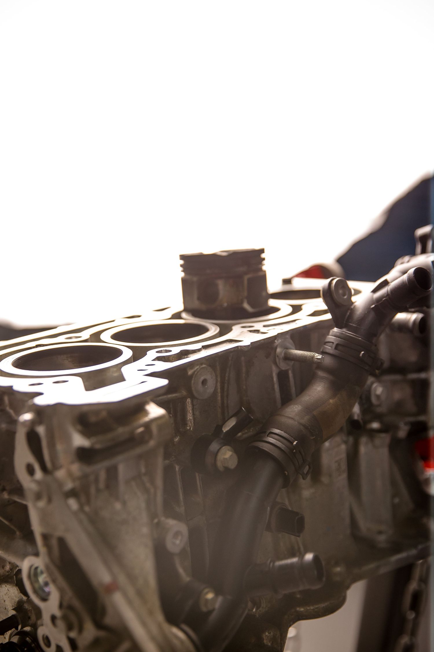 Close-up of a disassembled car engine block with visible pistons, cylinders, and coolant hoses during repair.