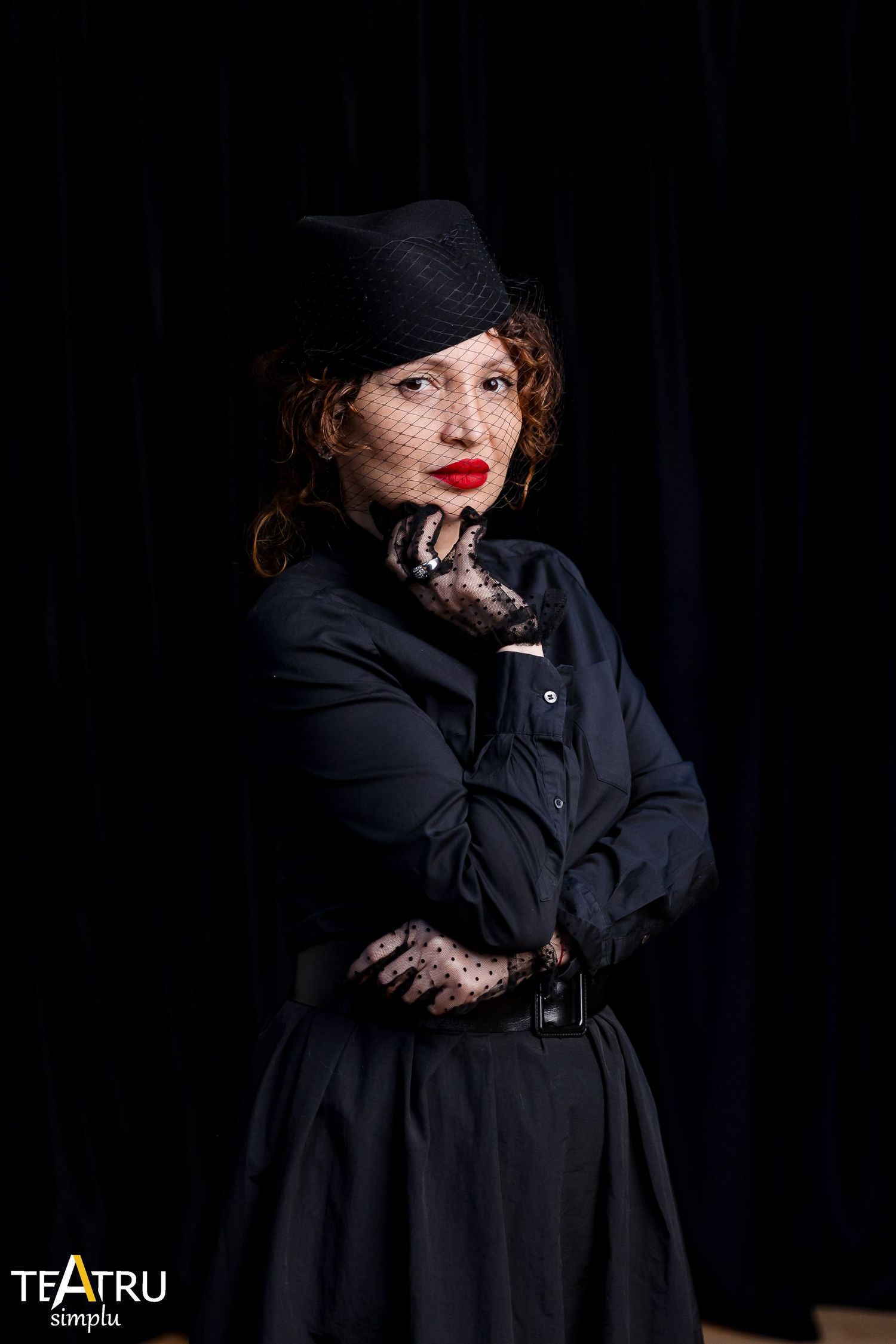 Woman in black dress, hat with veil, and lace gloves poses dramatically for Teatru Simplu theater production.