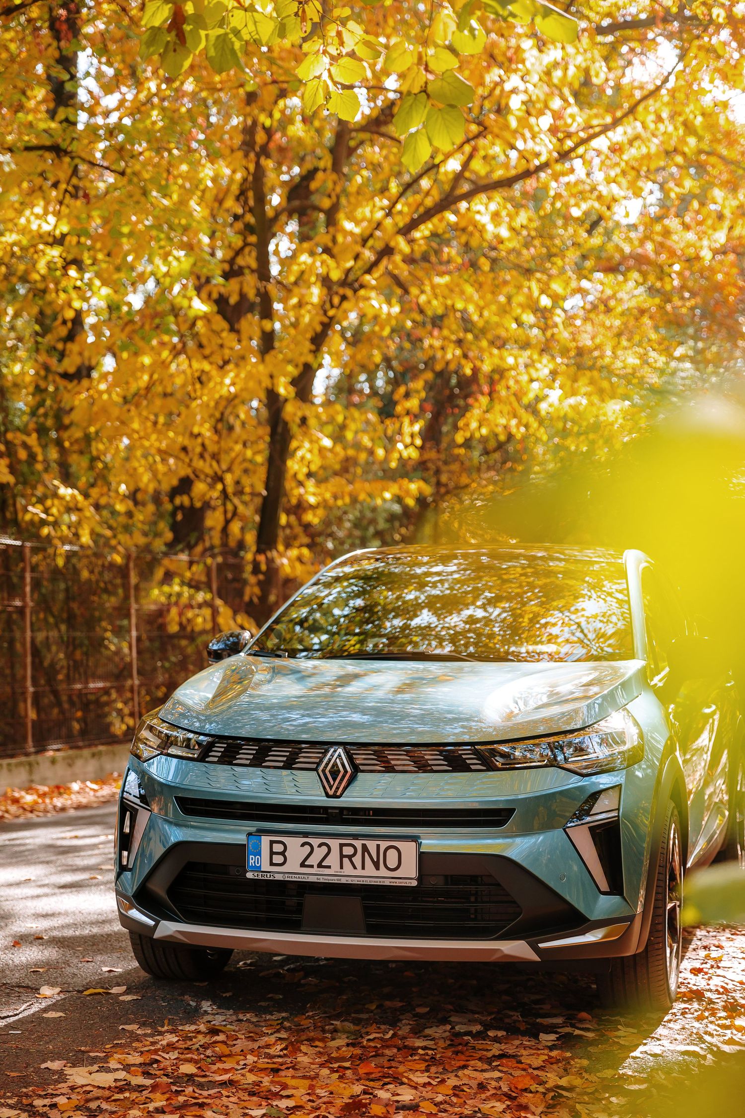 Renault SUV parked on a sunlit autumn road surrounded by golden yellow trees with fallen leaves.