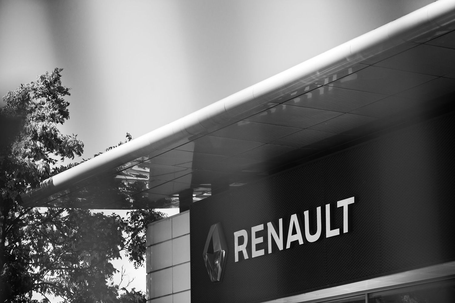 Black and white photo of a Renault dealership sign on a modern building facade with trees in the background.