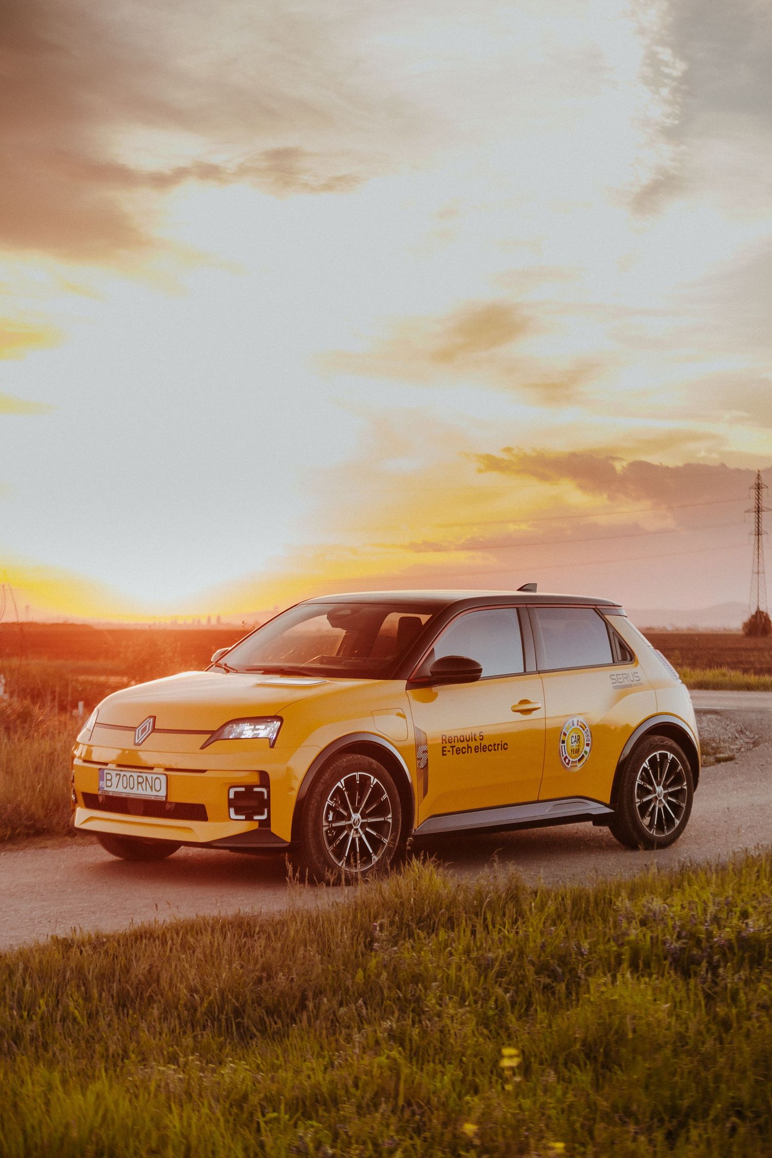 Yellow Renault 5 electric car parked on a rural road at golden sunset, with dramatic cloudy sky and green fields.