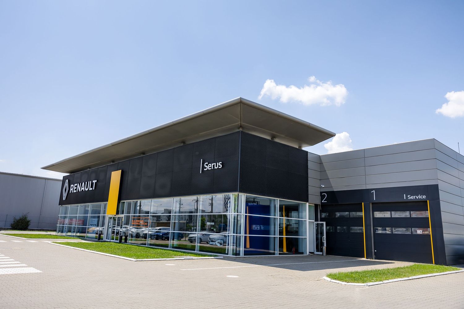 Renault Serus car dealership exterior with modern black facade, yellow accents, and spacious parking lot on a sunny day.