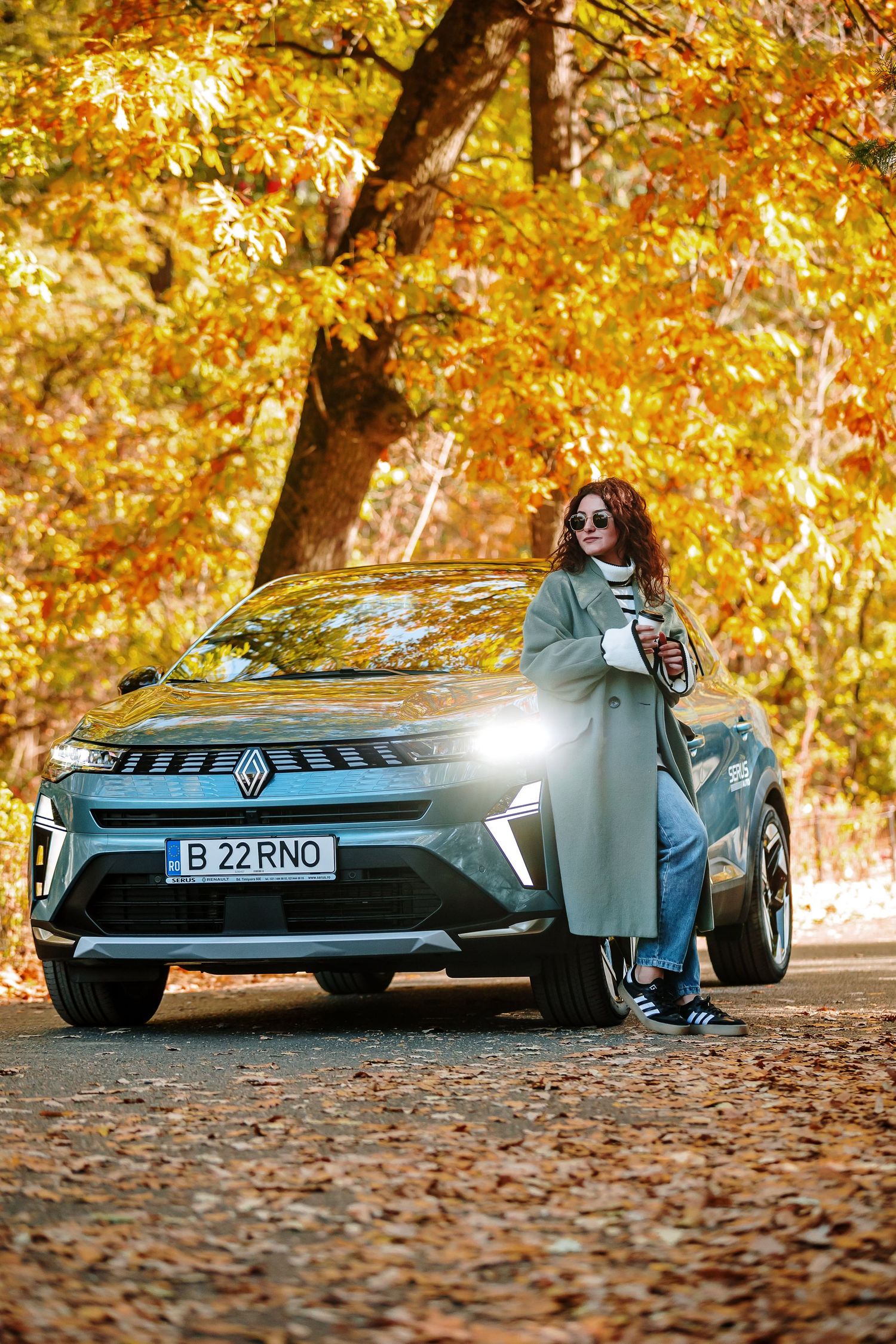 Woman leaning on a Renault SUV with Romanian license plate amid golden autumn foliage in a forest park.