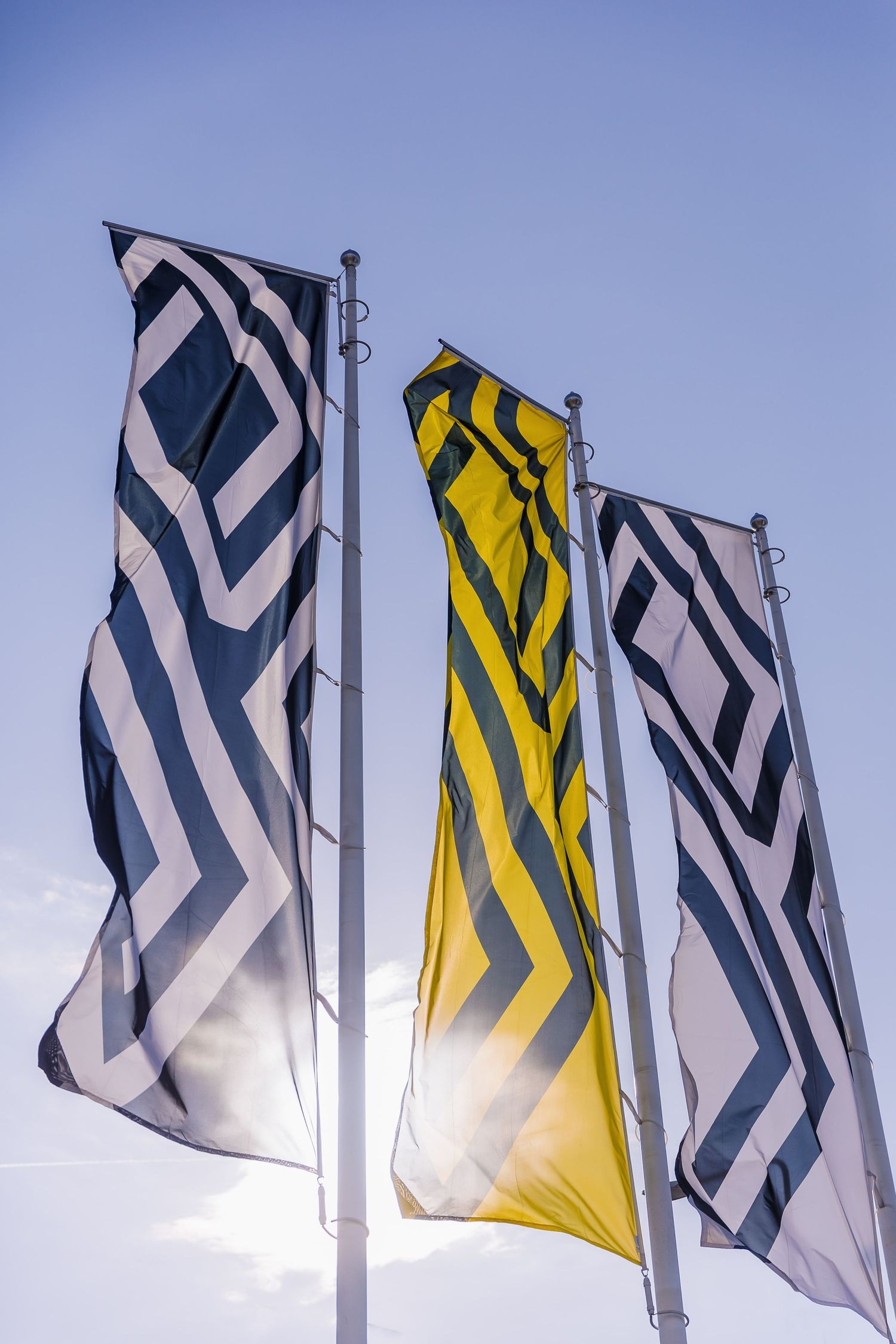 Three decorative flags with geometric chevron patterns in black, white, and yellow wave against a blue sky.