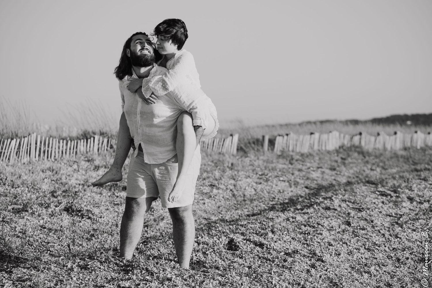 Couple sharing a playful piggyback ride on a beach in black and white photo.