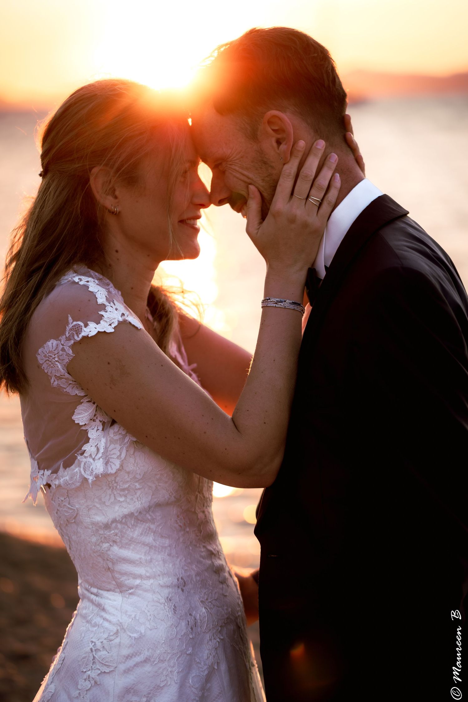 Newlyweds sharing intimate moment with foreheads touching during stunning beach sunset.