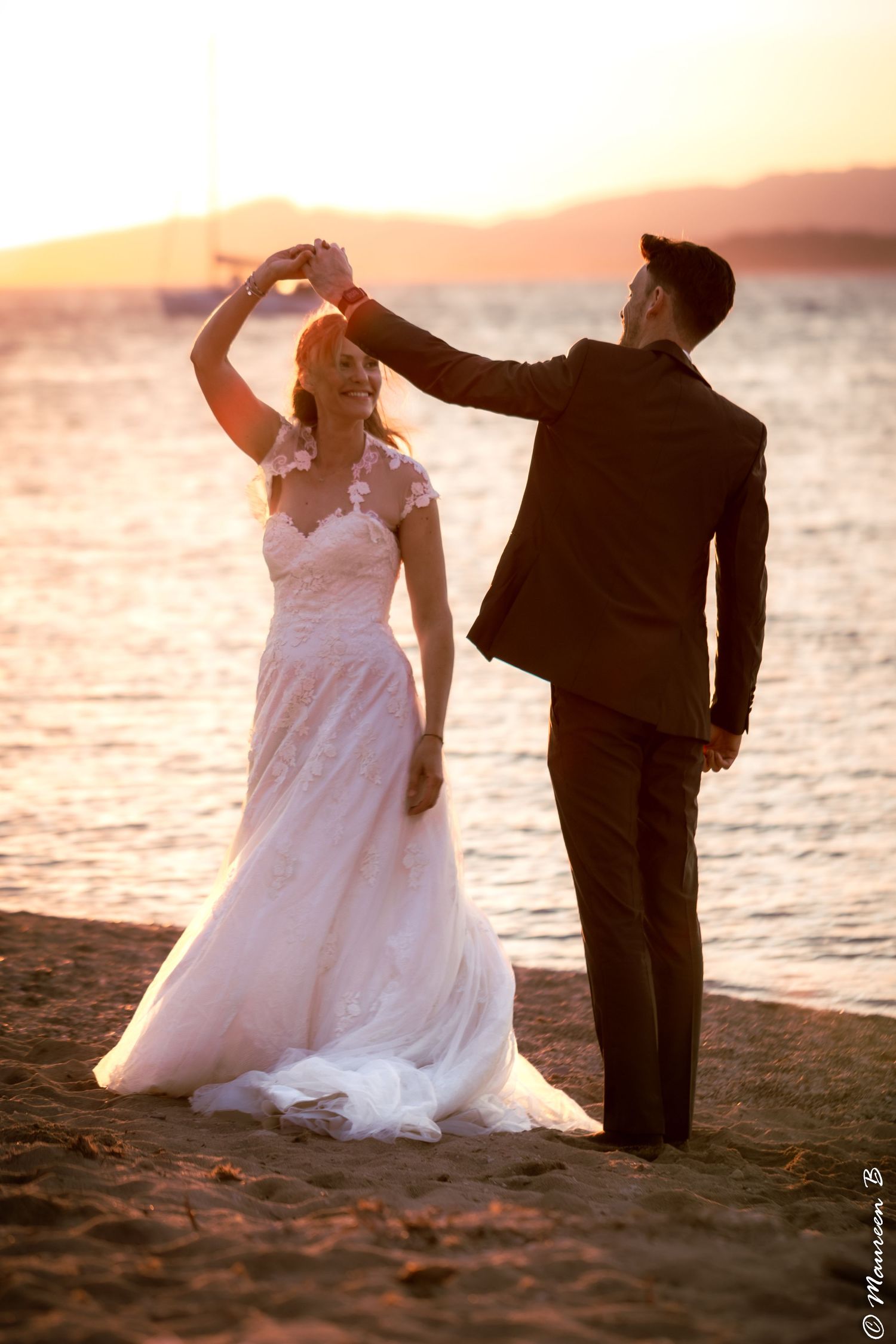 Groom spinning bride on sandy beach at golden sunset, bride laughing in lace wedding dress.