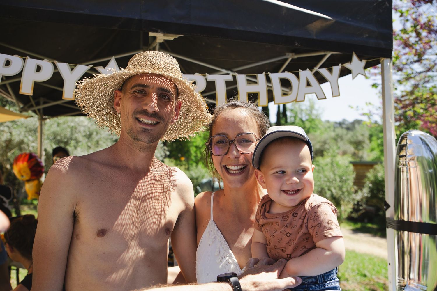 Happy family with parents in straw hats celebrating a birthday outdoors with their baby.