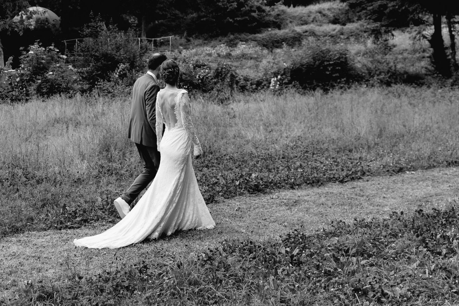 Black and white photo of a bride and groom walking together outdoors on their wedding day.