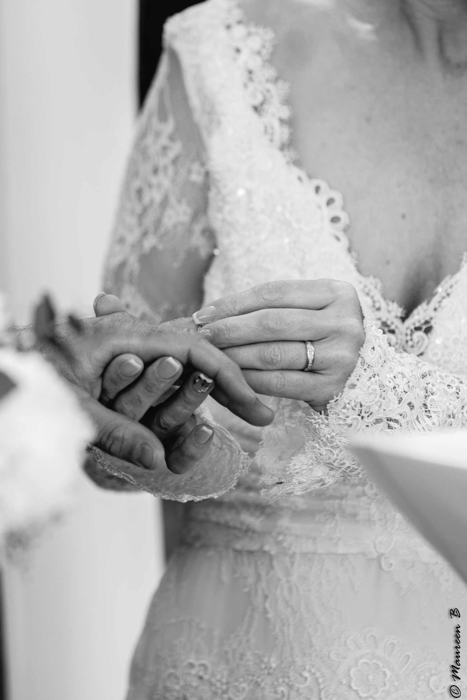 Black and white close-up of bride placing wedding ring on grooms finger during ceremony.