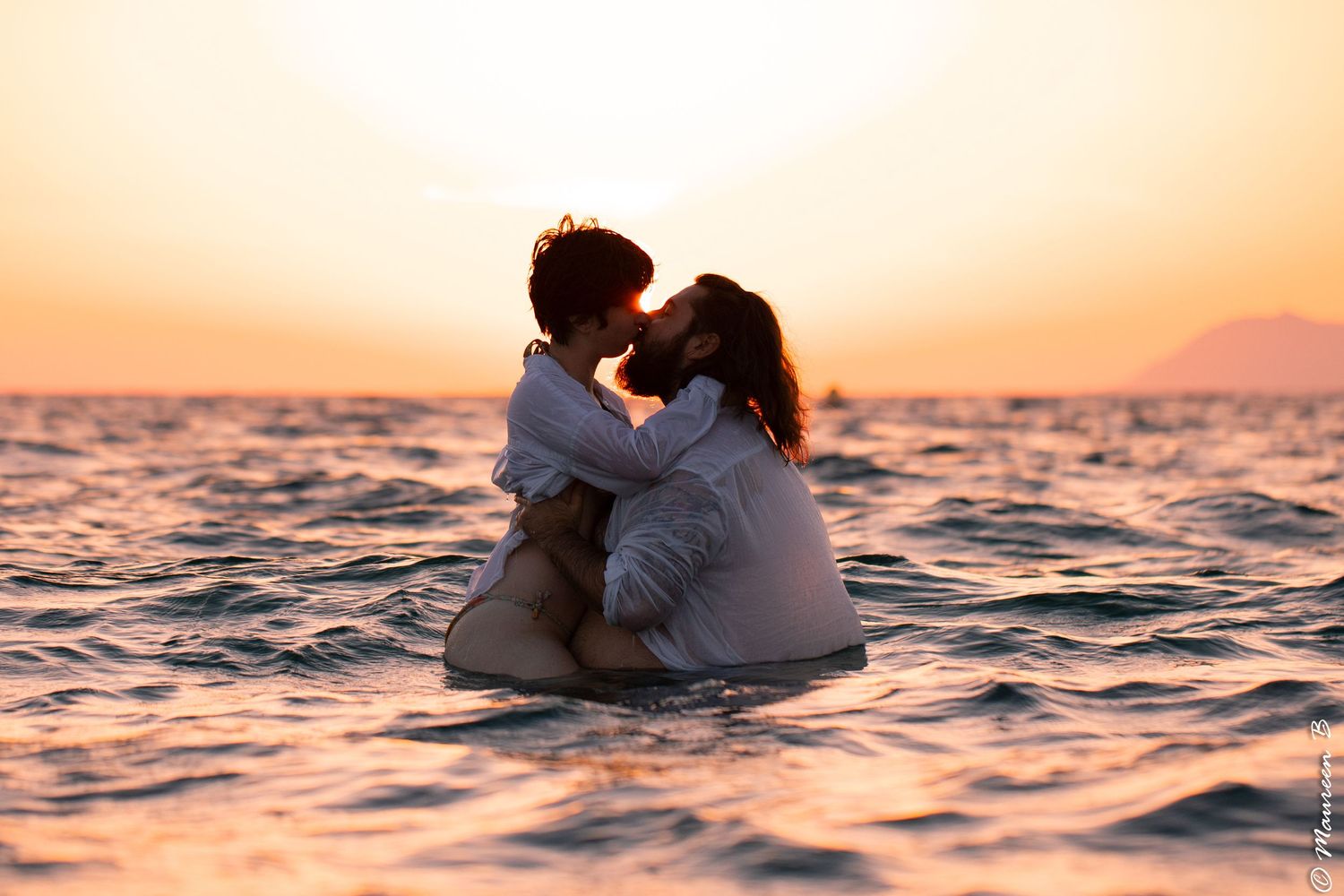 Couple kissing while standing together in the ocean at a warm golden sunset.