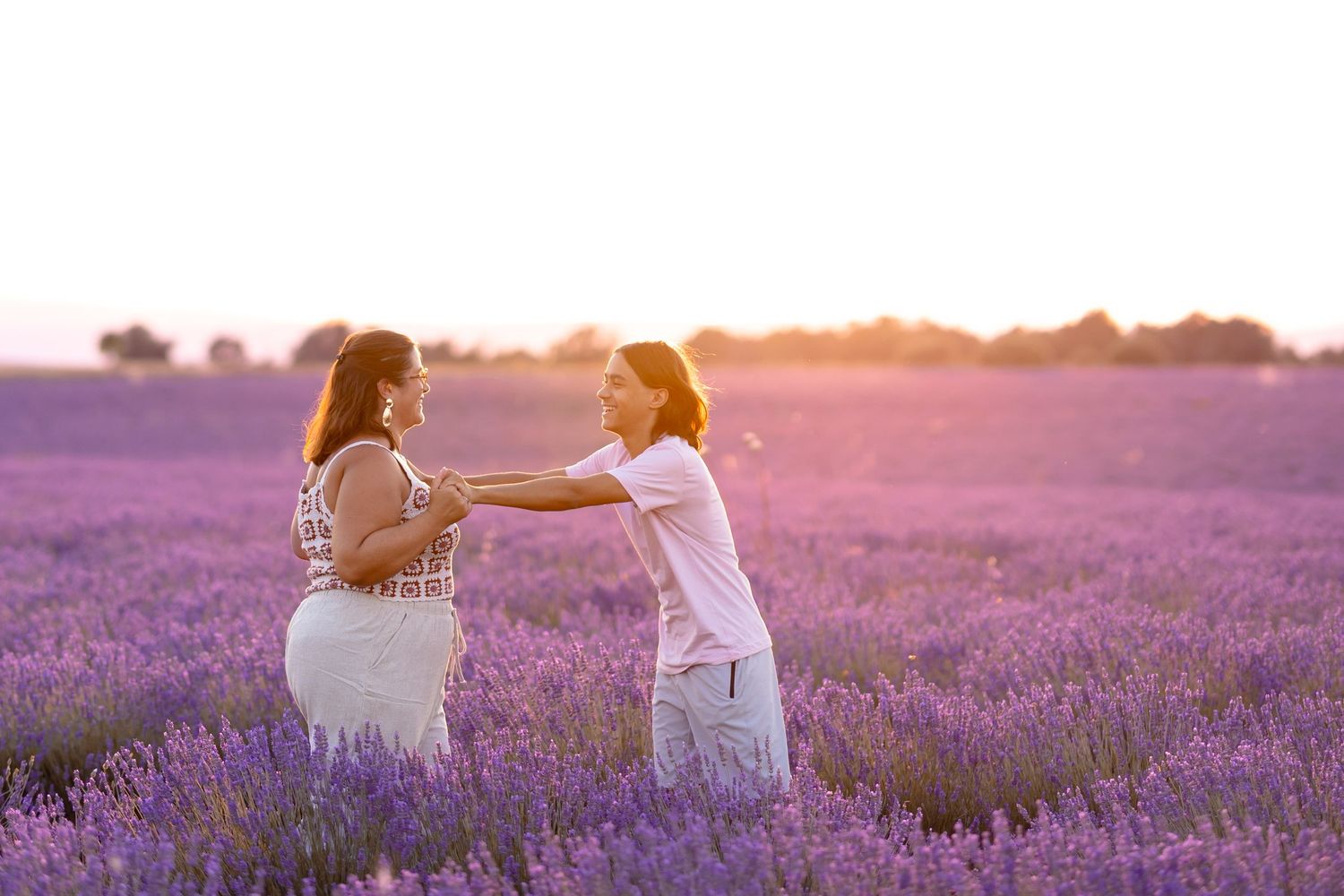 Couple dancing and holding hands in a blooming lavender field at sunset.