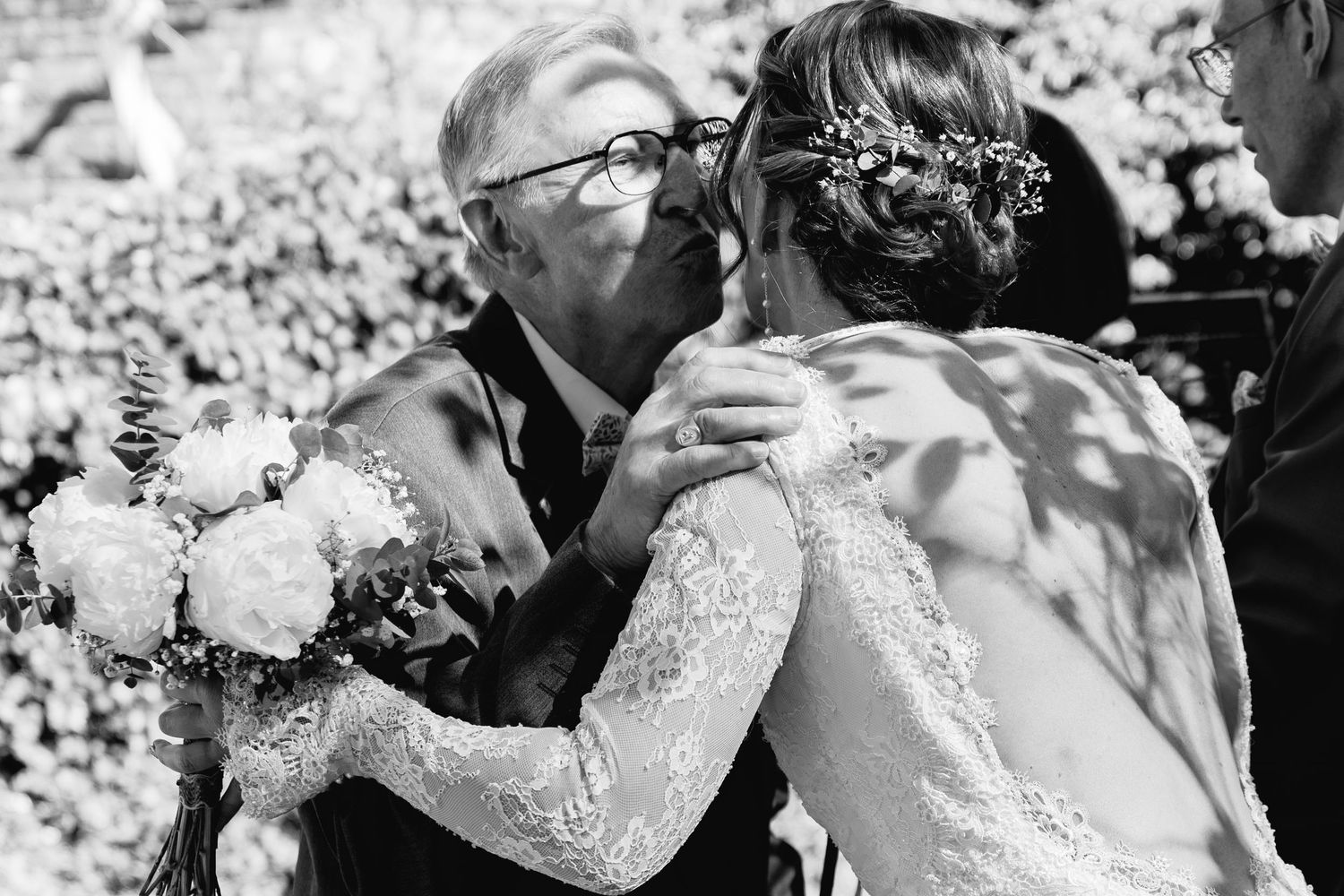 Black and white photo of a bride embracing an older man, likely her father, holding a bouquet at a wedding ceremony.
