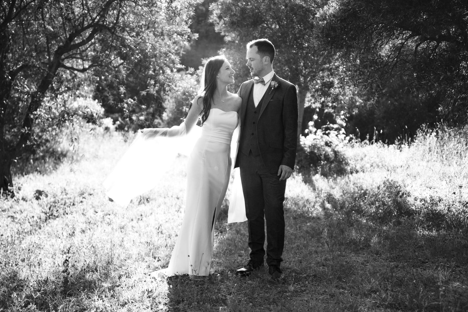 Black and white photo of a bride and groom holding hands in a lush outdoor setting on their wedding day.