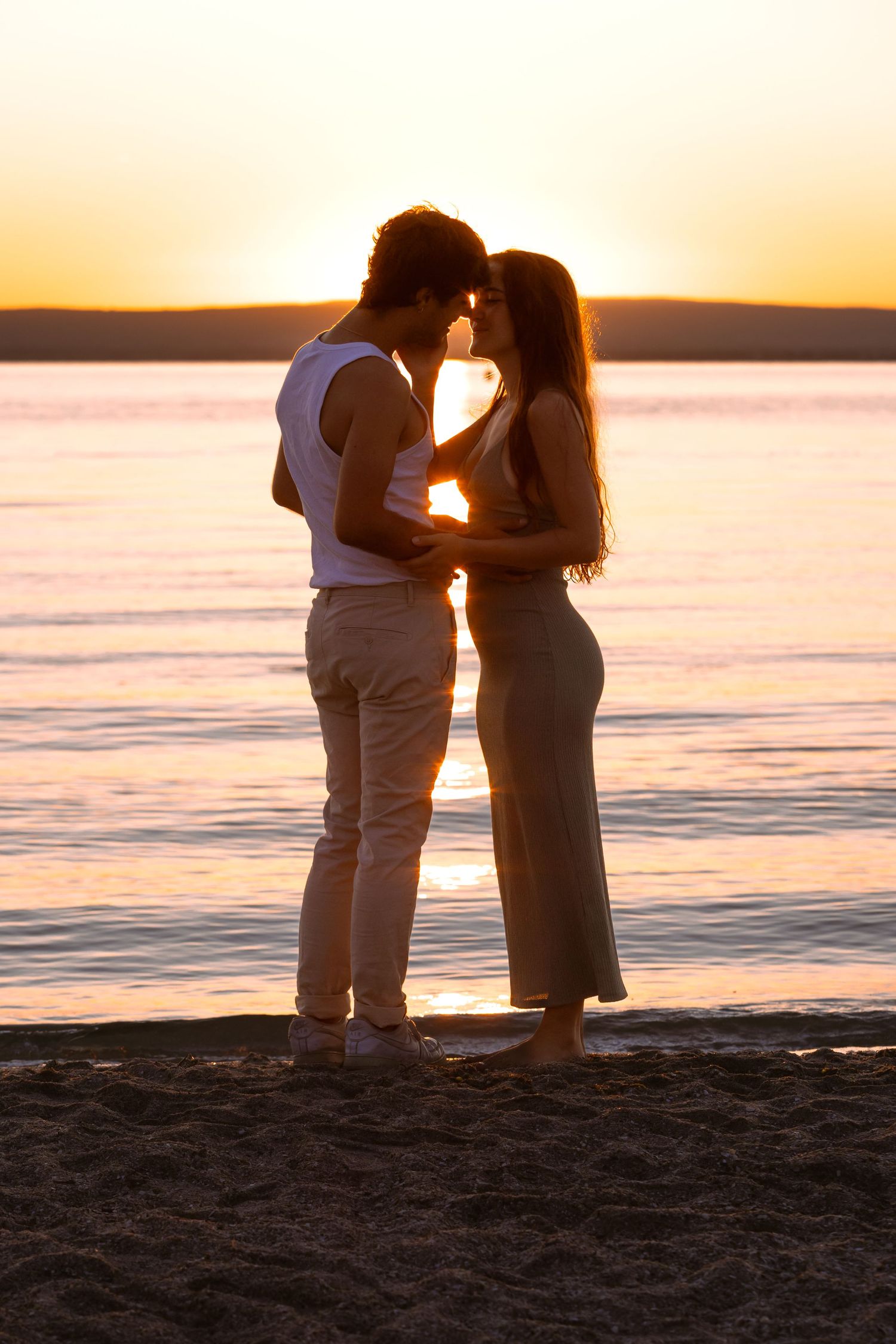 Romantic couple silhouetted against a golden sunset embracing on a peaceful beach shoreline.