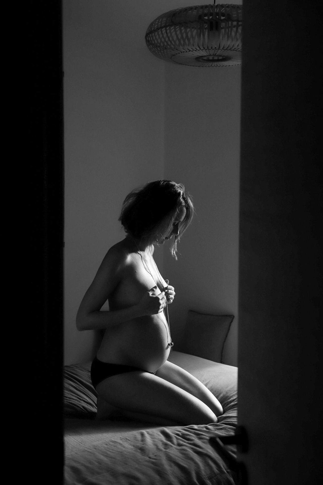 Pregnant woman kneeling on bed in black and white maternity boudoir photo.