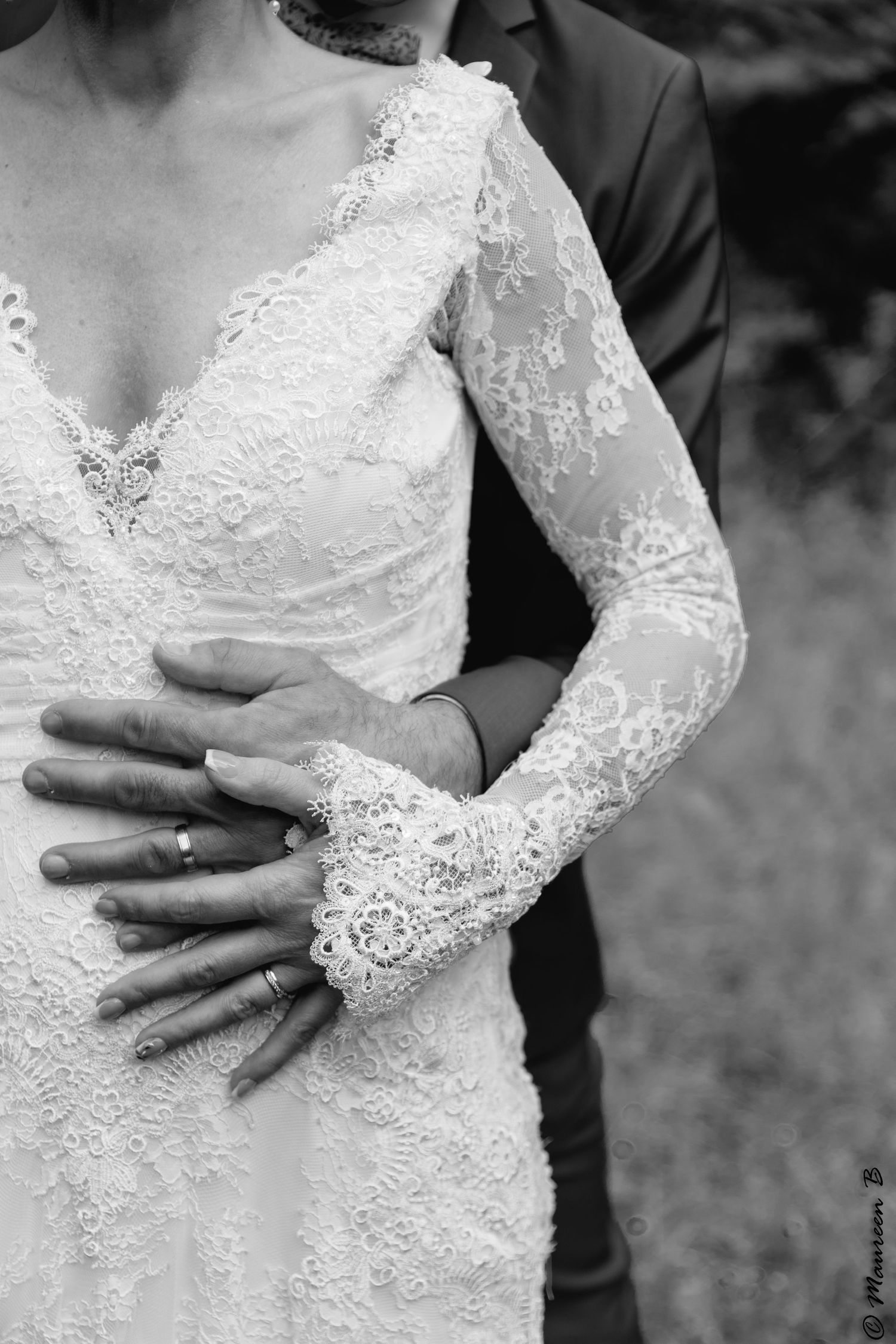 Black and white photo of bride in lace wedding gown with groom's hand on her waist, both wearing wedding rings.