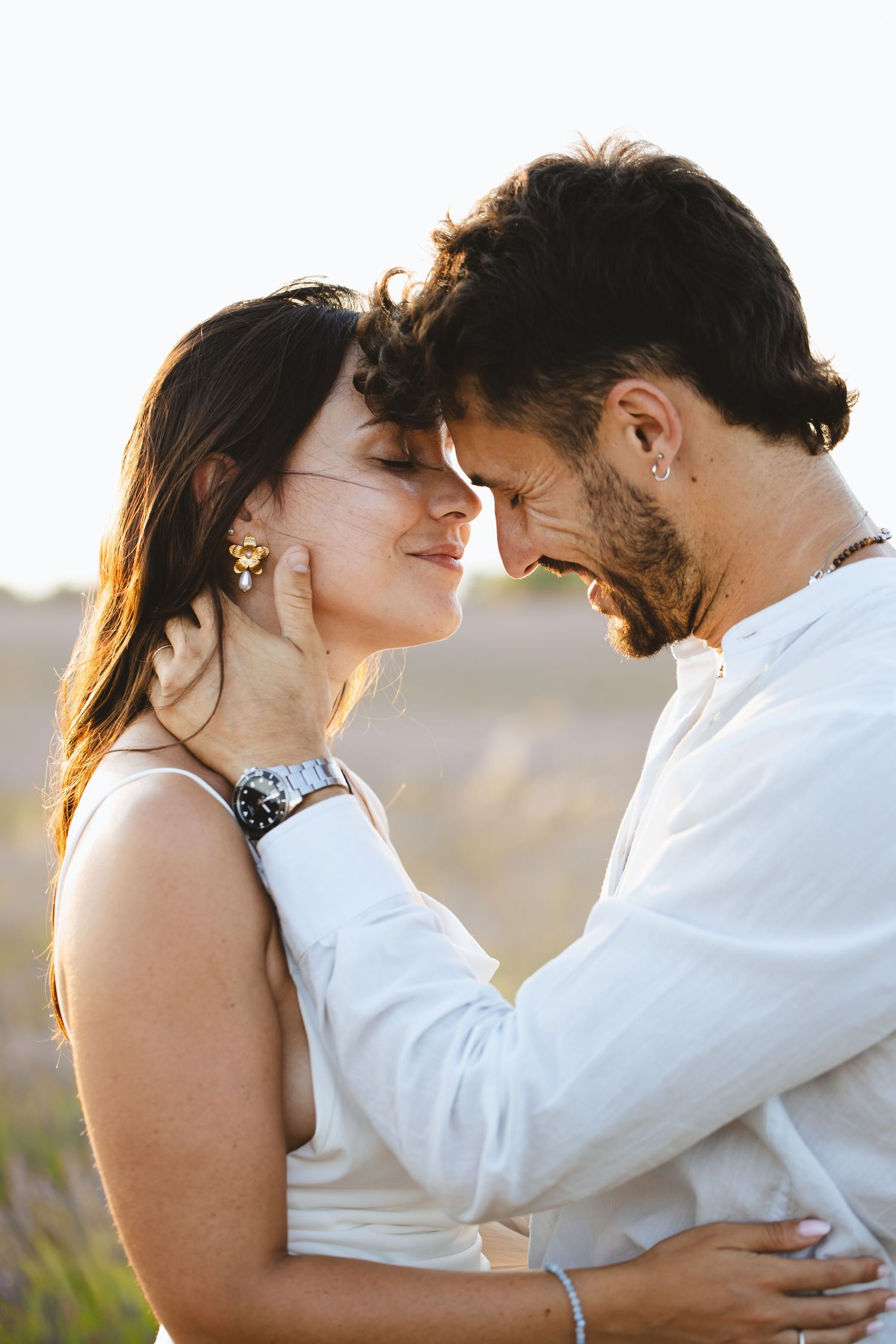 Romantic couple touching foreheads tenderly in warm golden sunlight outdoors.