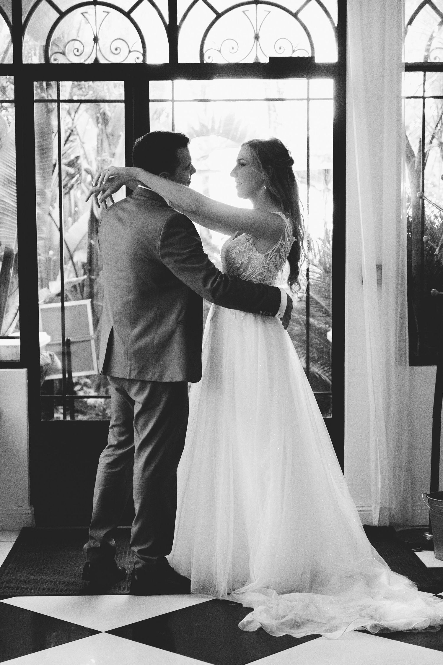 Bride and groom sharing romantic embrace near ornate doors in elegant black and white wedding portrait.