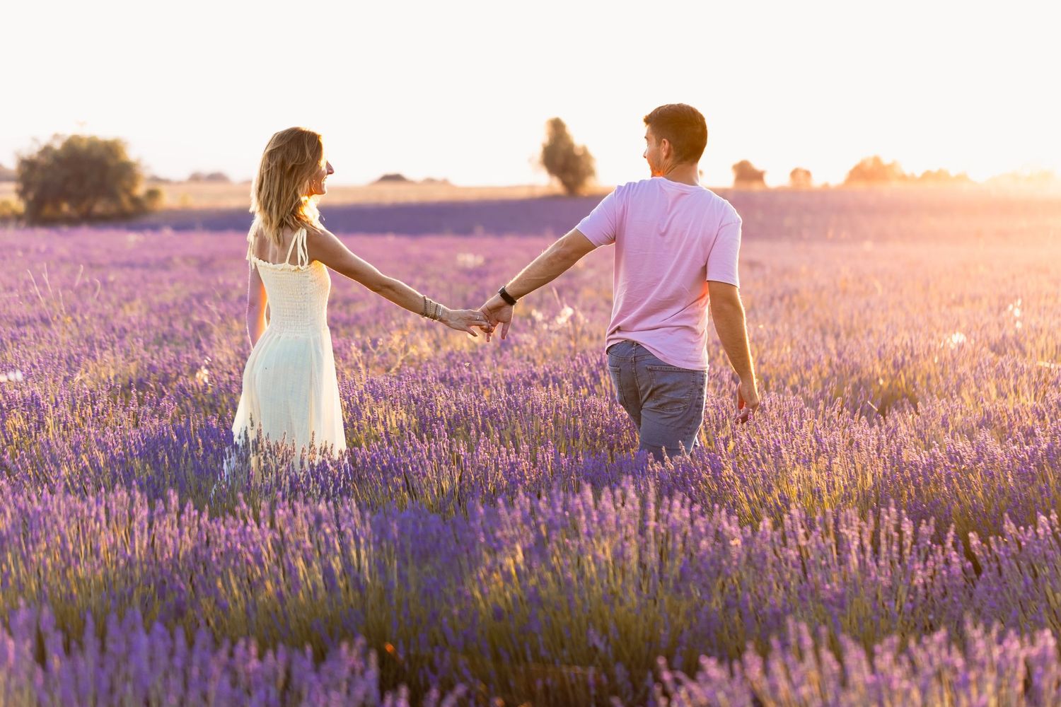 Couple holding hands walking through a beautiful blooming lavender field during golden hour sunset.