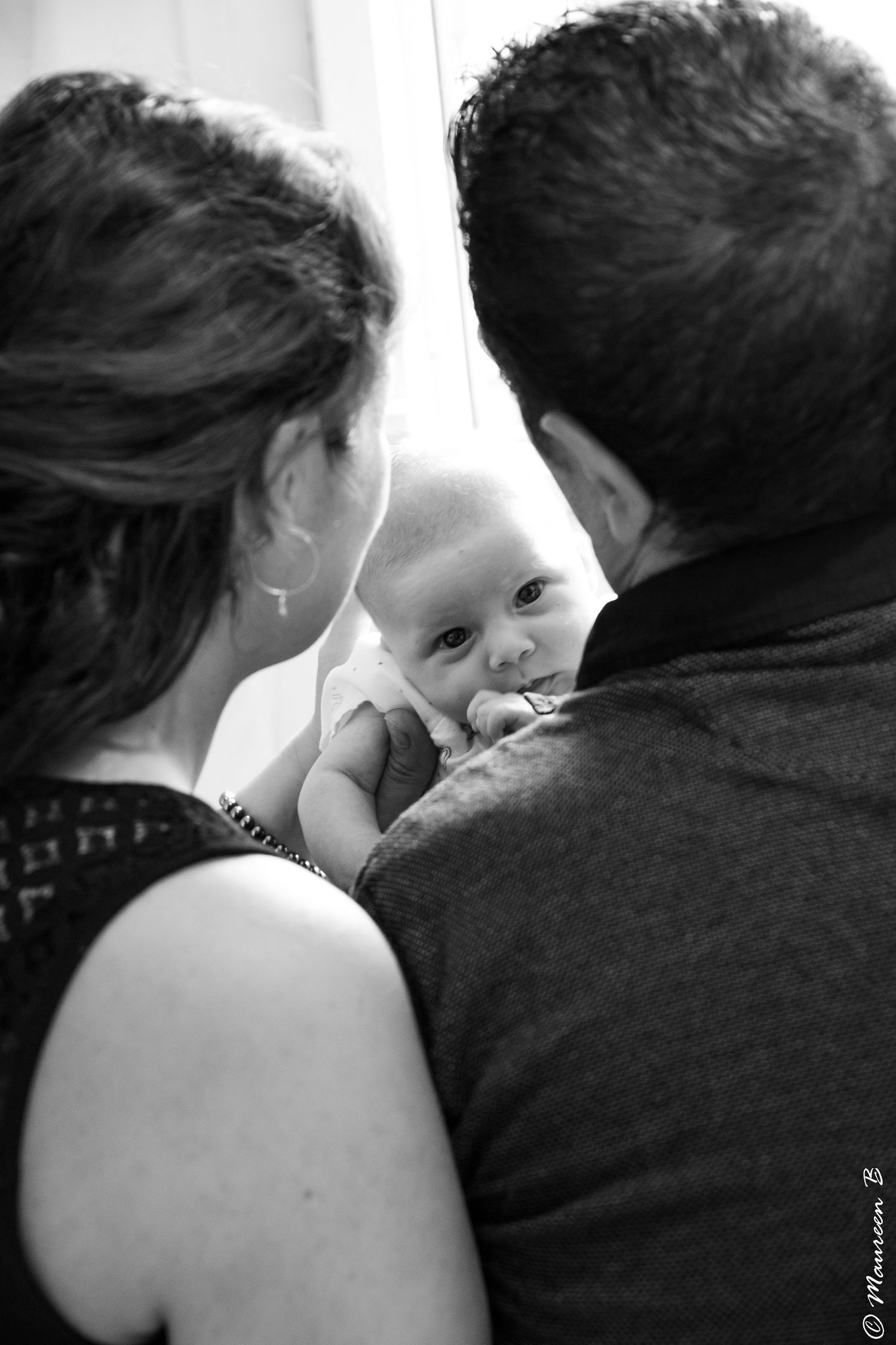 New parents lovingly hold their alert newborn baby in a tender black and white portrait.