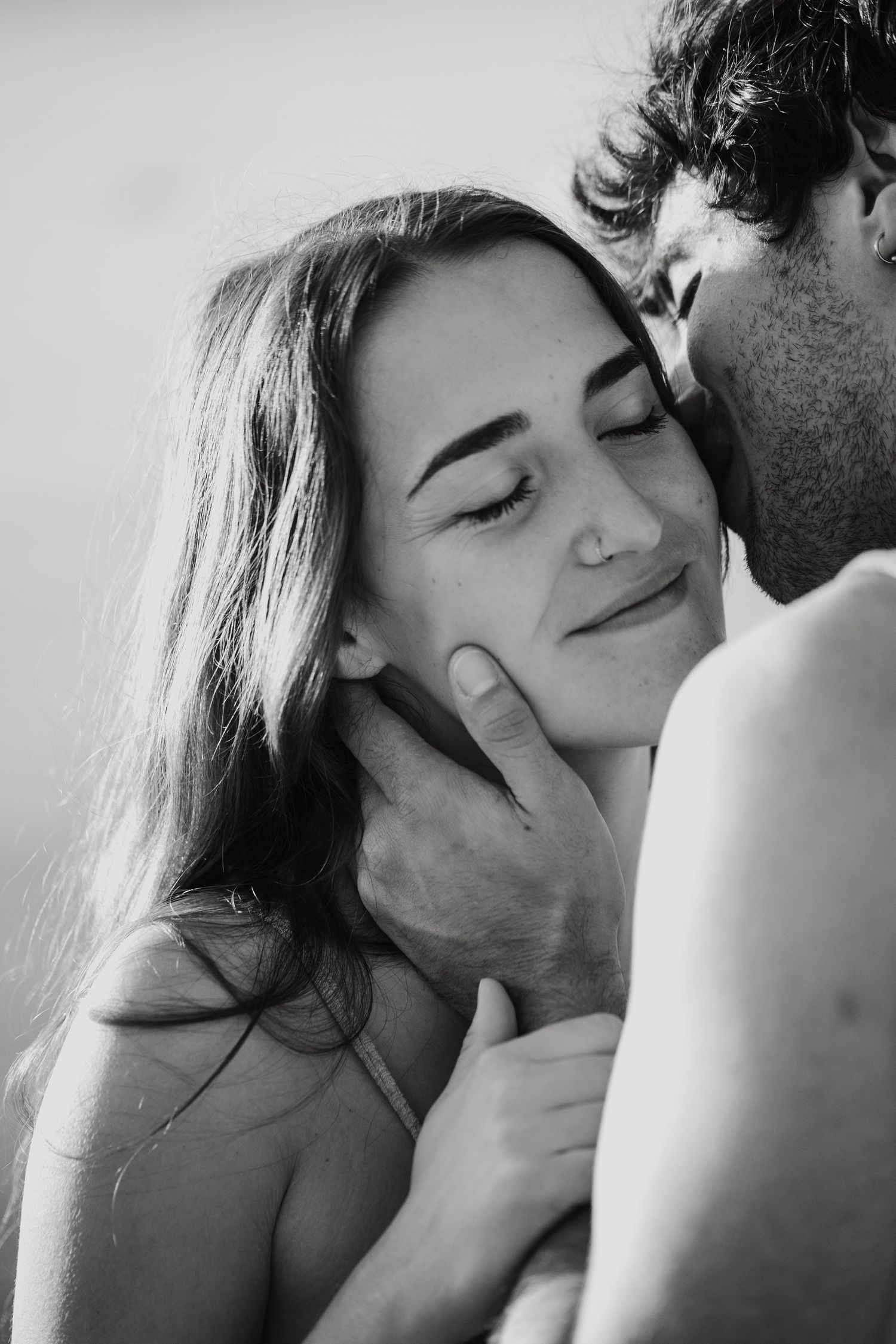 Black and white photo of a couple sharing a tender moment, man gently cupping womans face as she smiles with eyes closed.