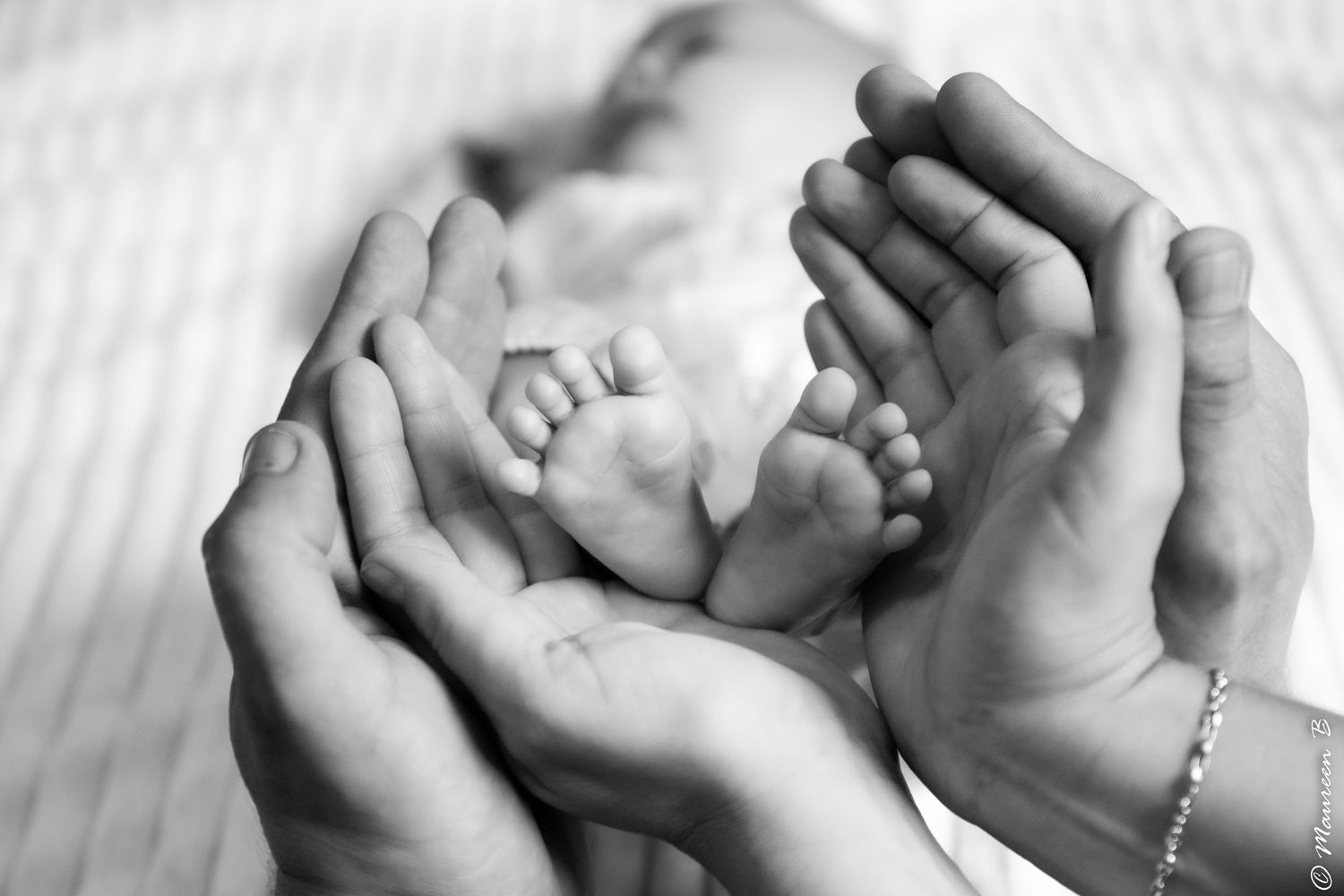 Parents cradle their newborns tiny feet gently in their hands in black and white.