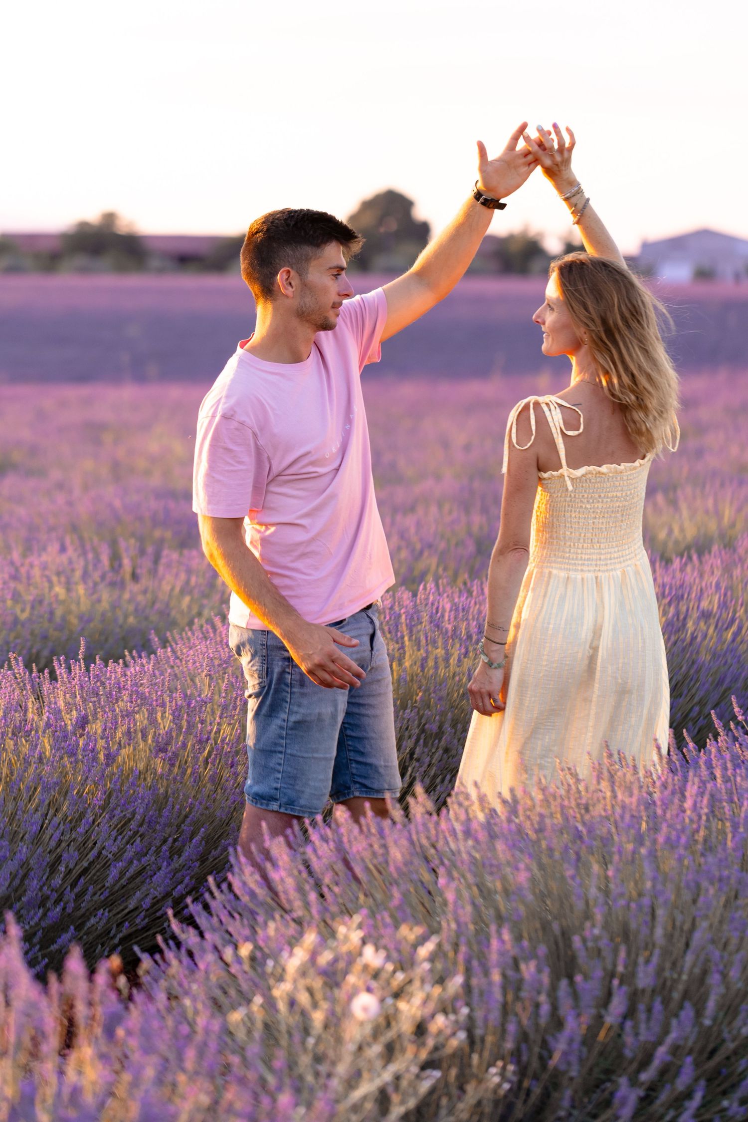 Happy couple dancing together in a vibrant purple lavender field during a warm golden sunset.