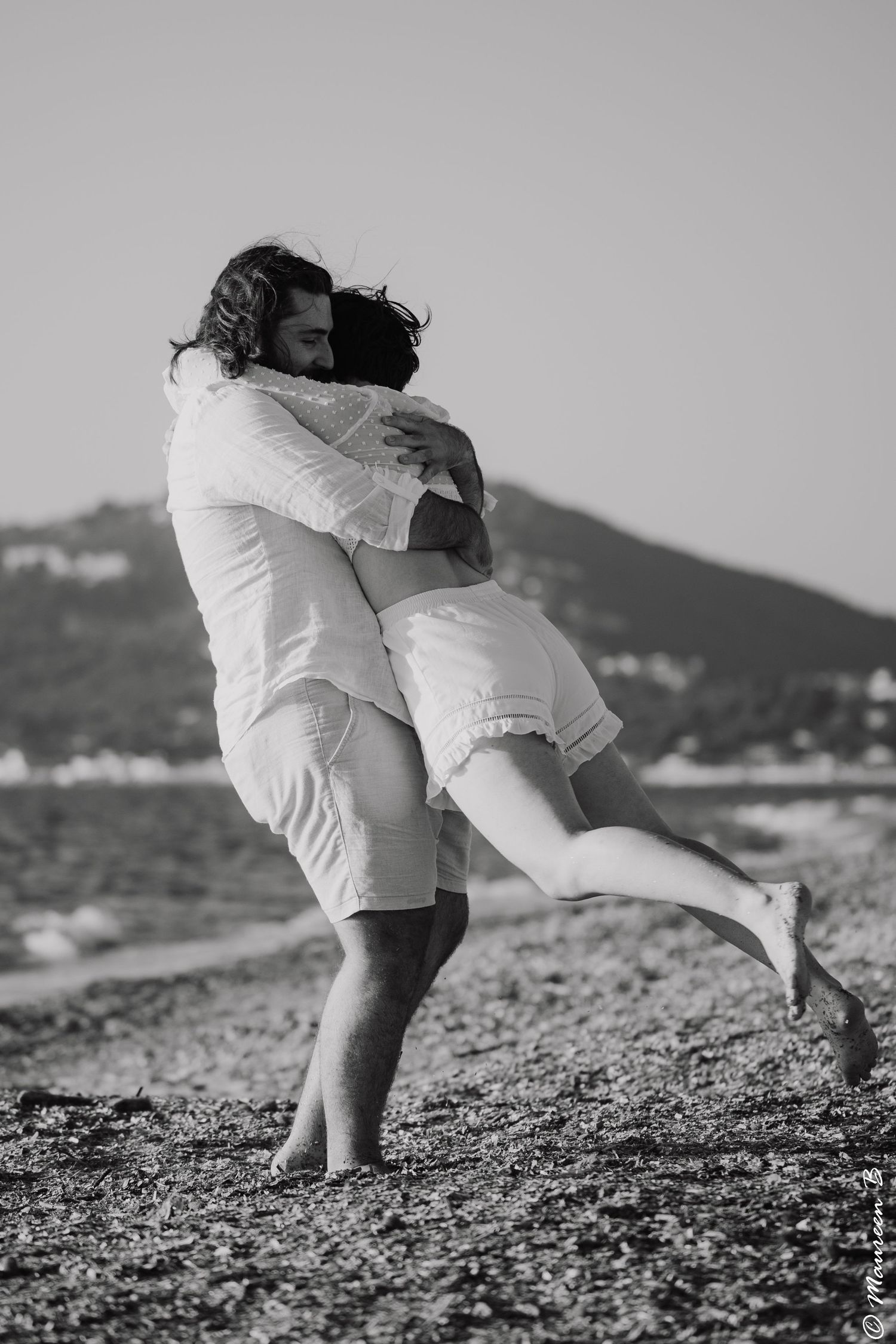 Black and white photo of a man lifting and hugging a woman on a rocky beach.