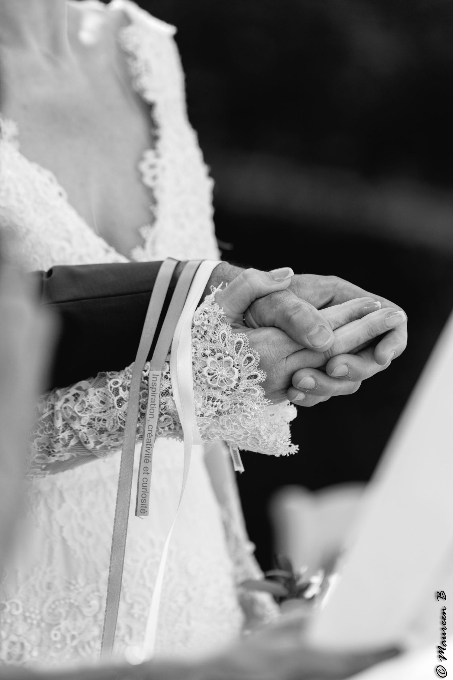 Close-up black and white photo of bride and groom holding hands during wedding ceremony.
