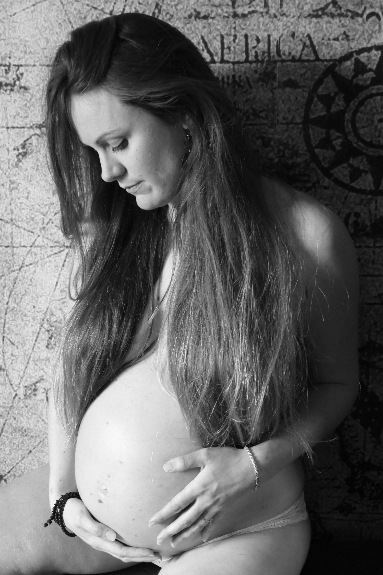 Black and white portrait of pregnant woman with long hair cradling her baby bump near world map.